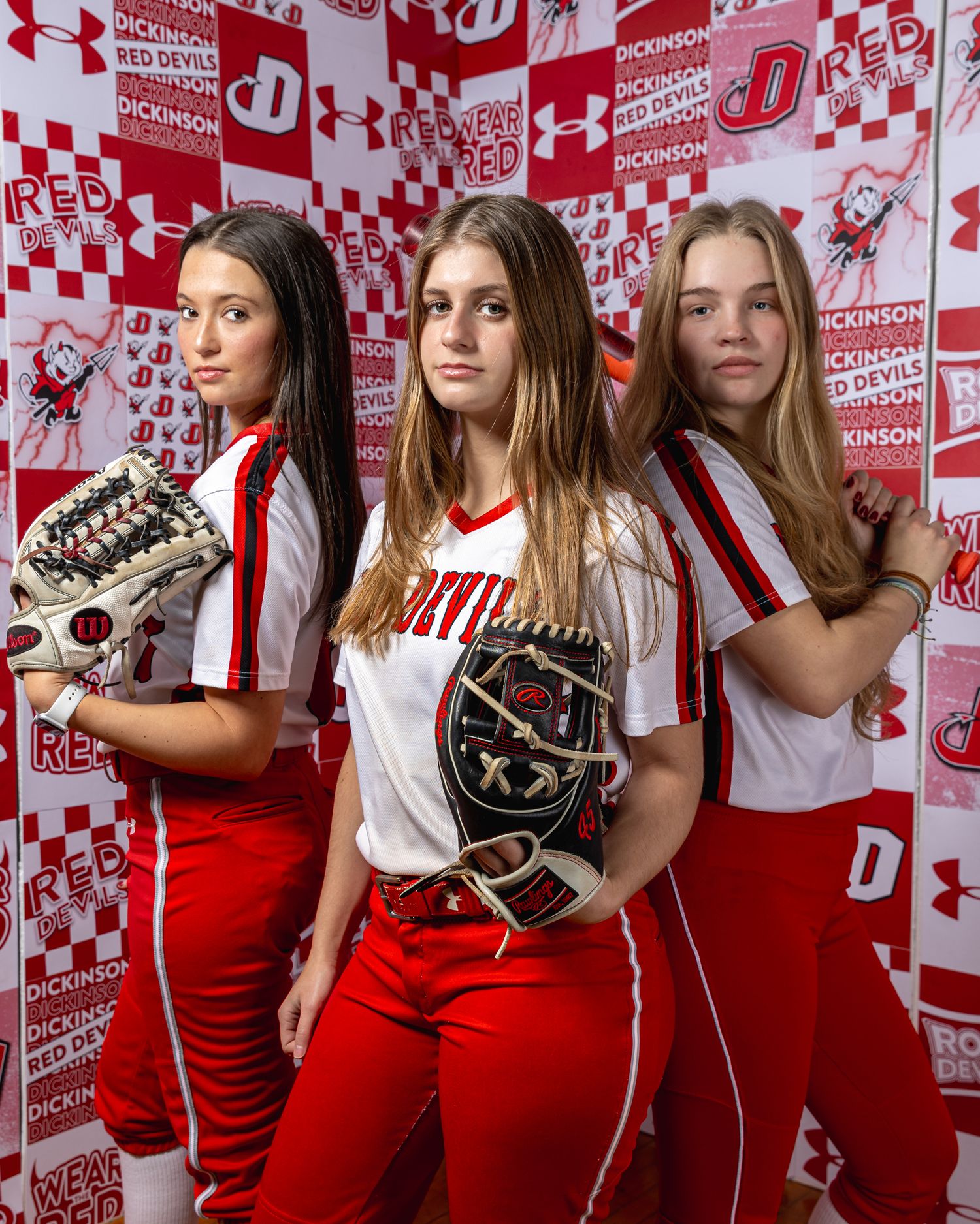 A group in red and white athletic uniforms poses against a branded Under Armour backdrop with checkered pattern.