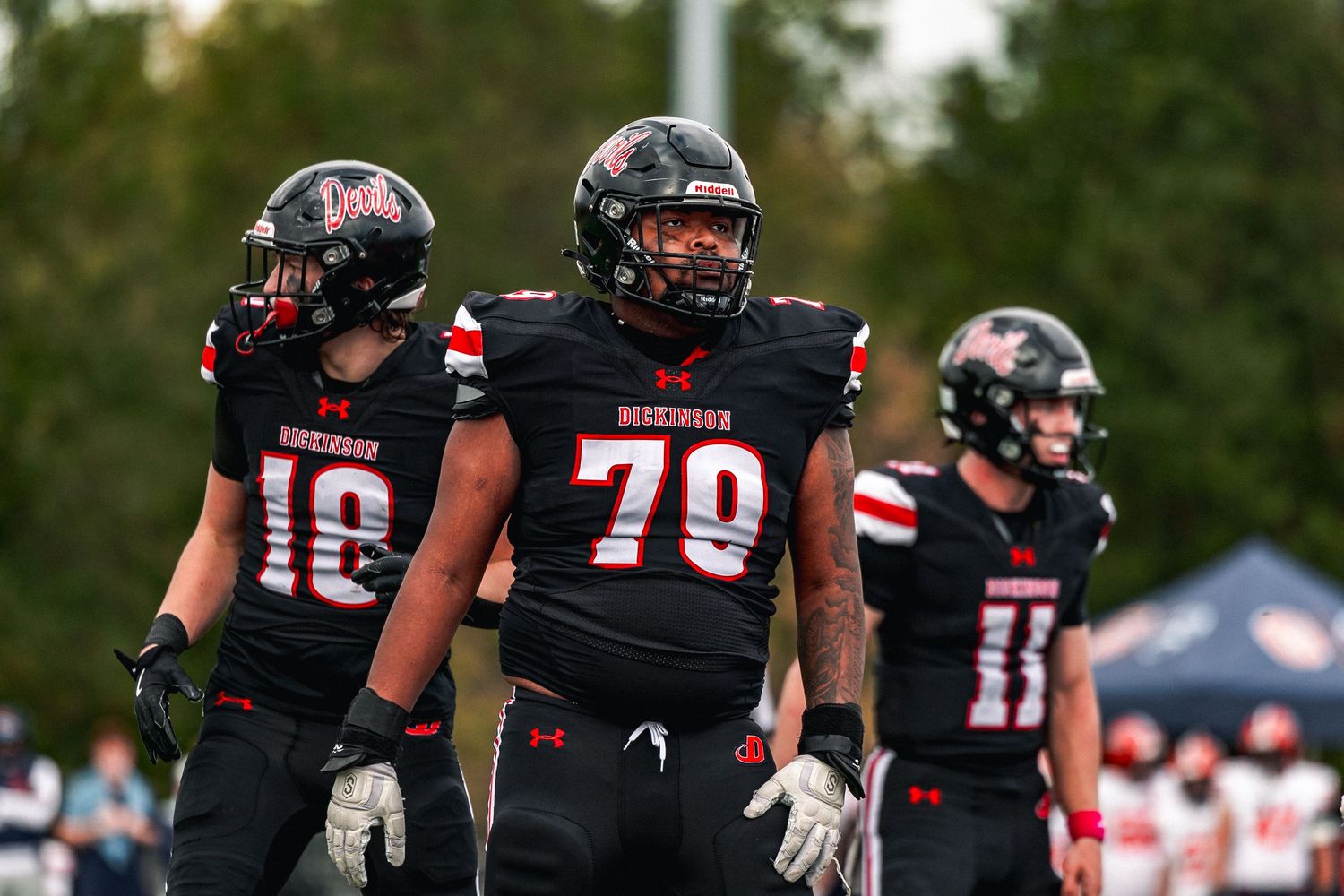 Football players in black uniforms celebrate during a game with fans and tents visible in the background.
