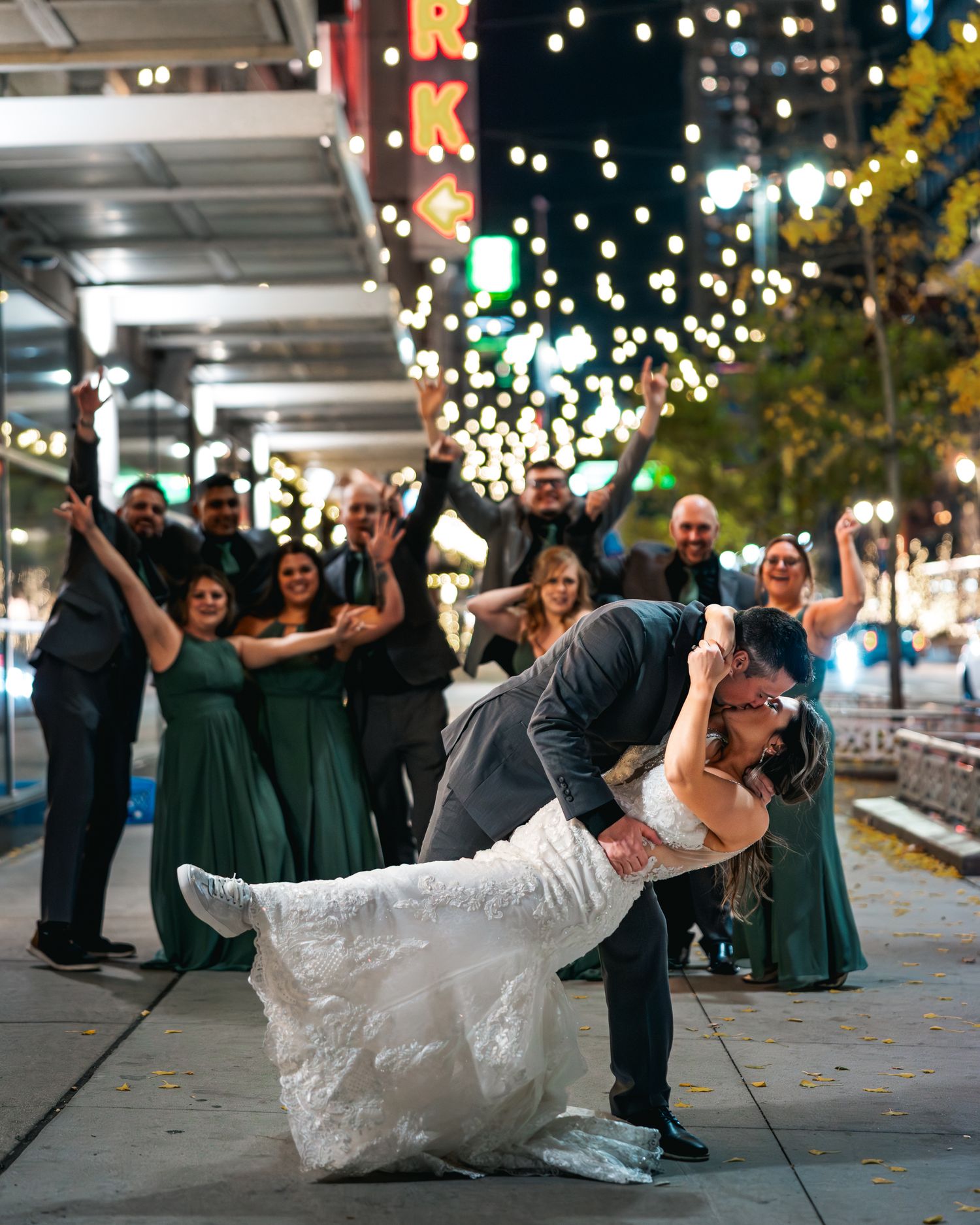 A sequence of wedding party photos showing playful dips and poses on an illuminated city sidewalk at night.