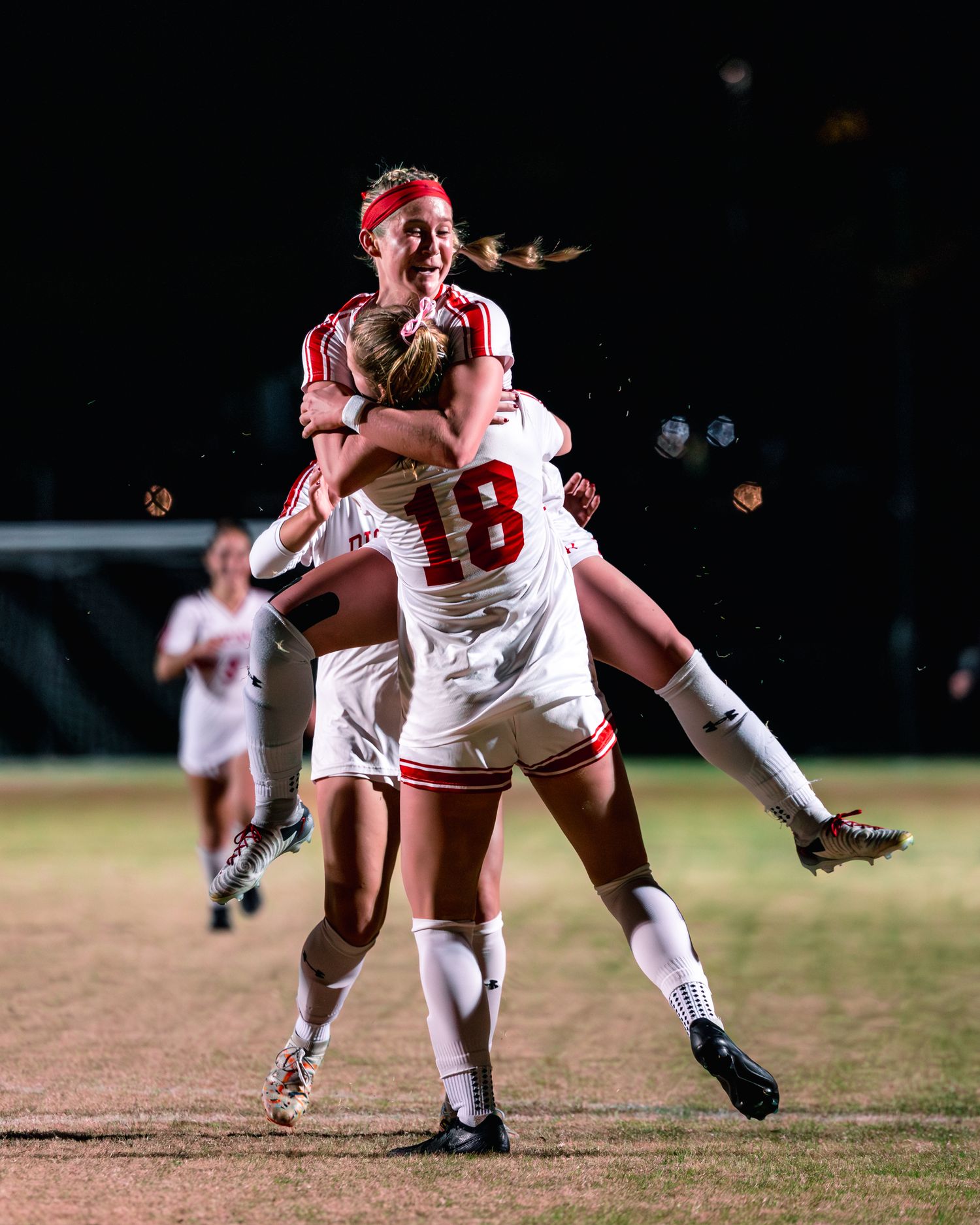 A softball player in a white uniform and red cap dives to catch a ball during a night game.