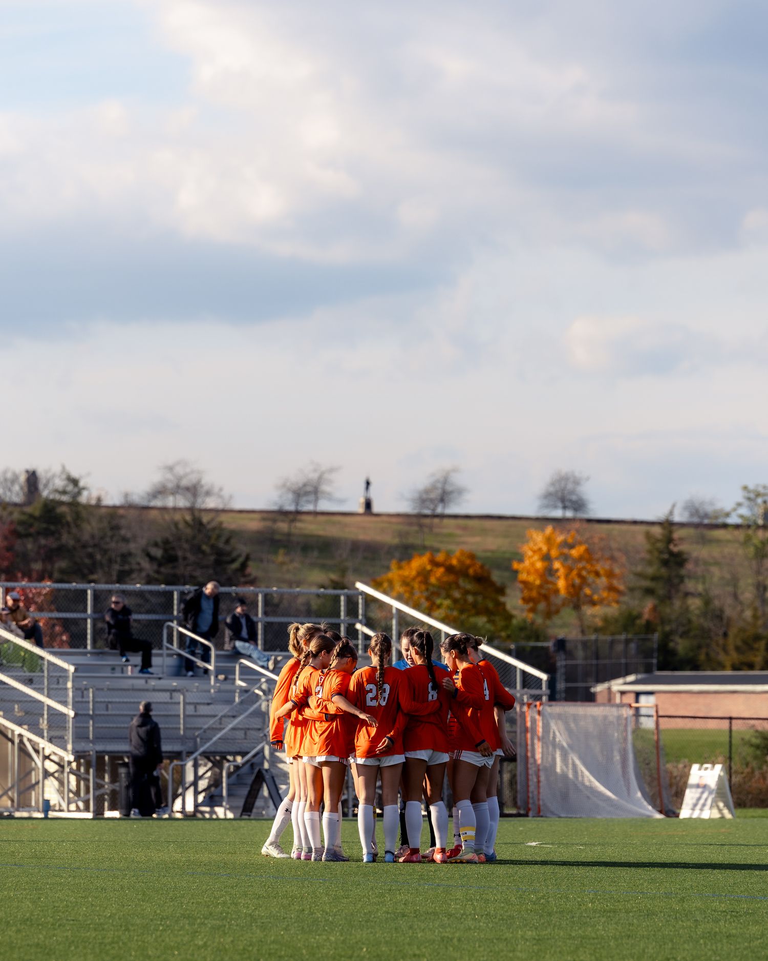 Soccer team huddles together on a green grass field with white goal posts visible in the background.