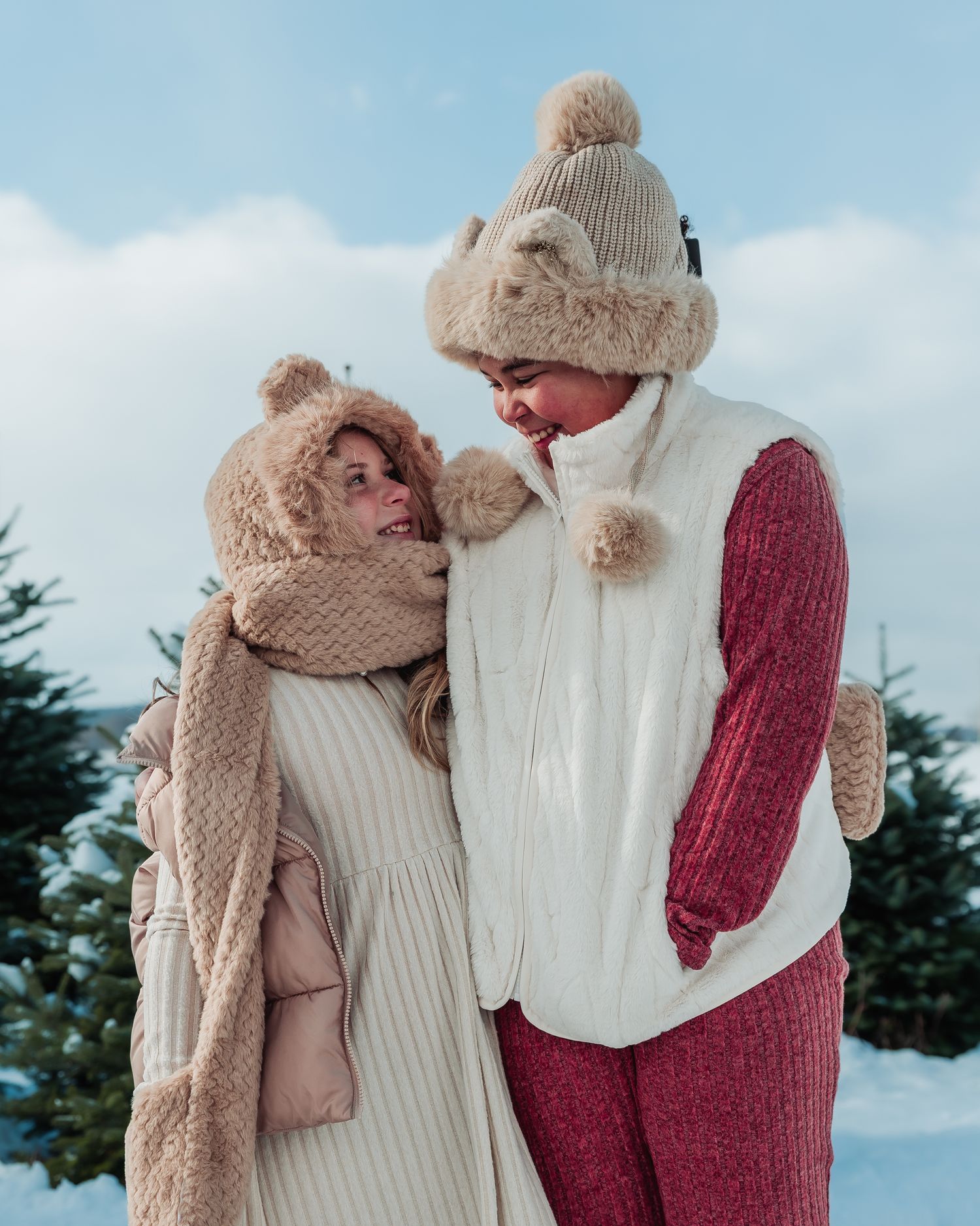 A couple in warm winter clothing embraces in a snowy outdoor setting wearing cozy knit sweaters and hats.