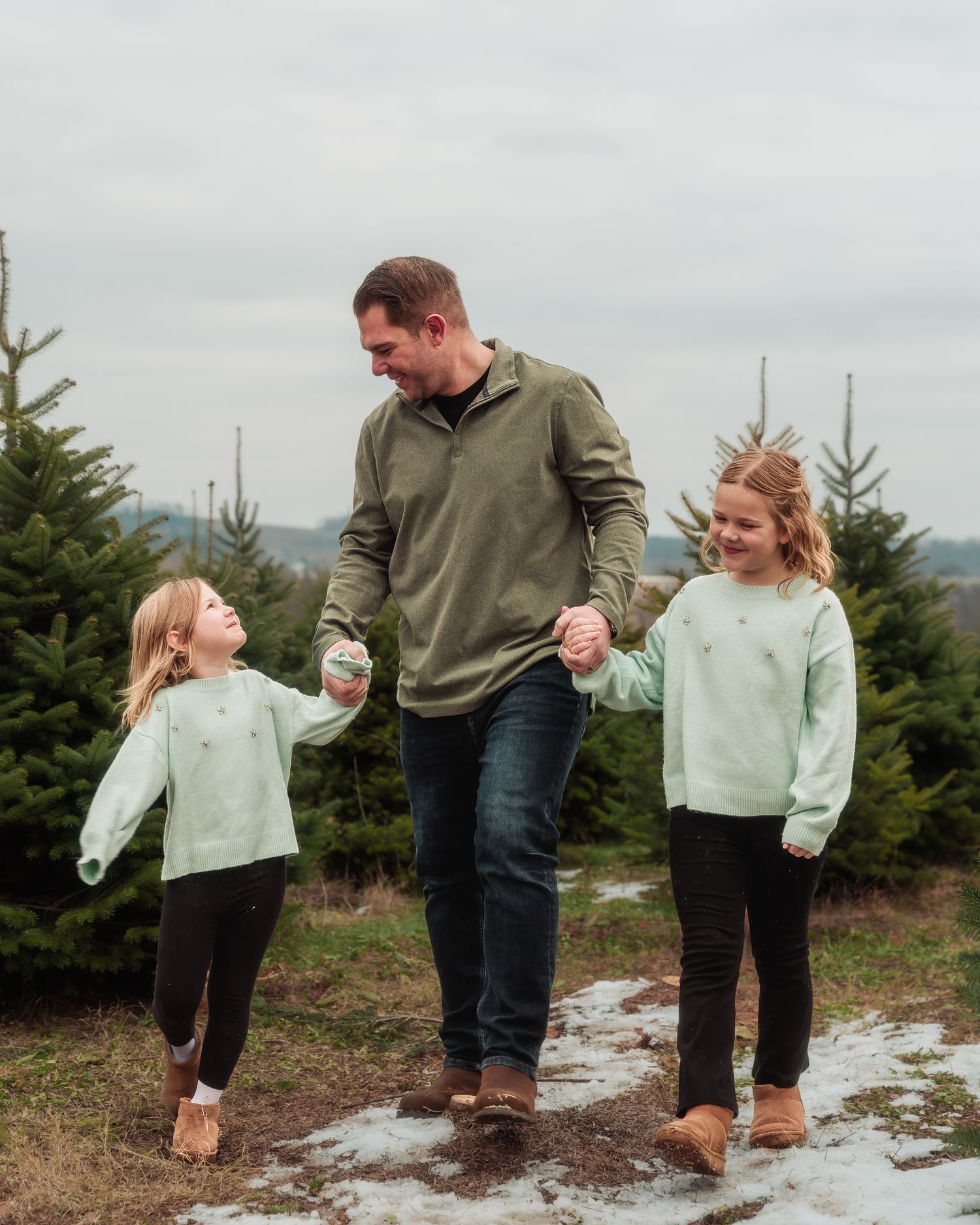 Family members splash in puddles together at a Christmas tree farm on an overcast day.