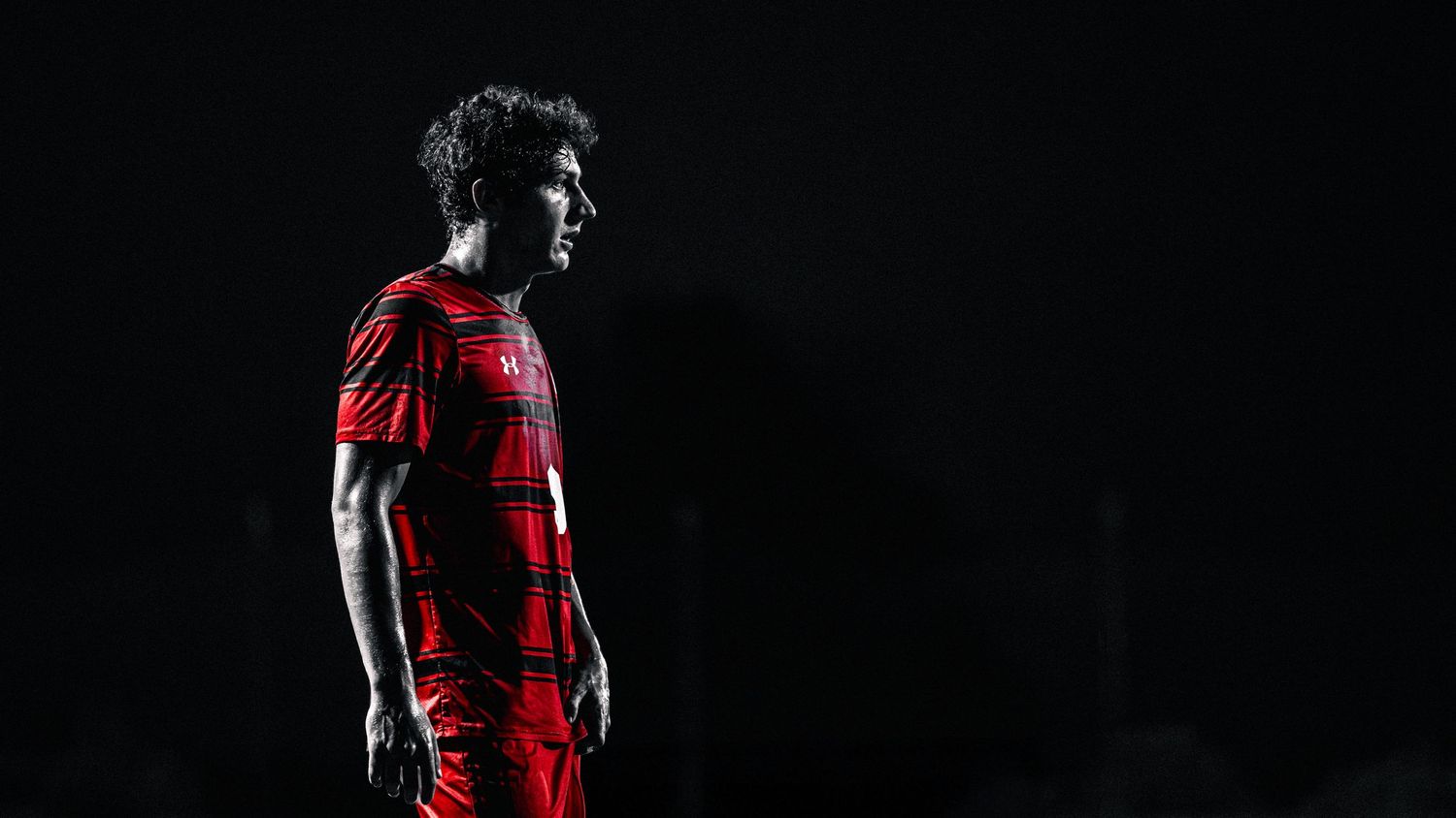 Dramatic silhouette of a soccer player in a red jersey standing against a dark background.