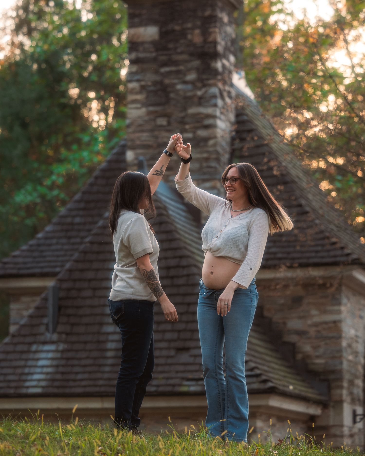 Two people dancing together on a grassy lawn at sunset with a rustic building in the background.
