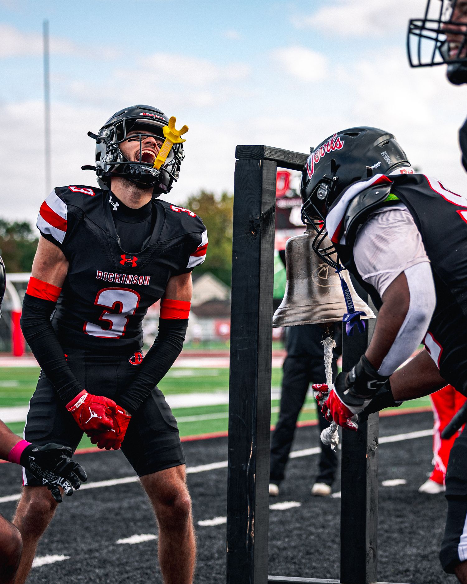 Football players in black and red uniforms line up in three-point stances at the line of scrimmage during practice.