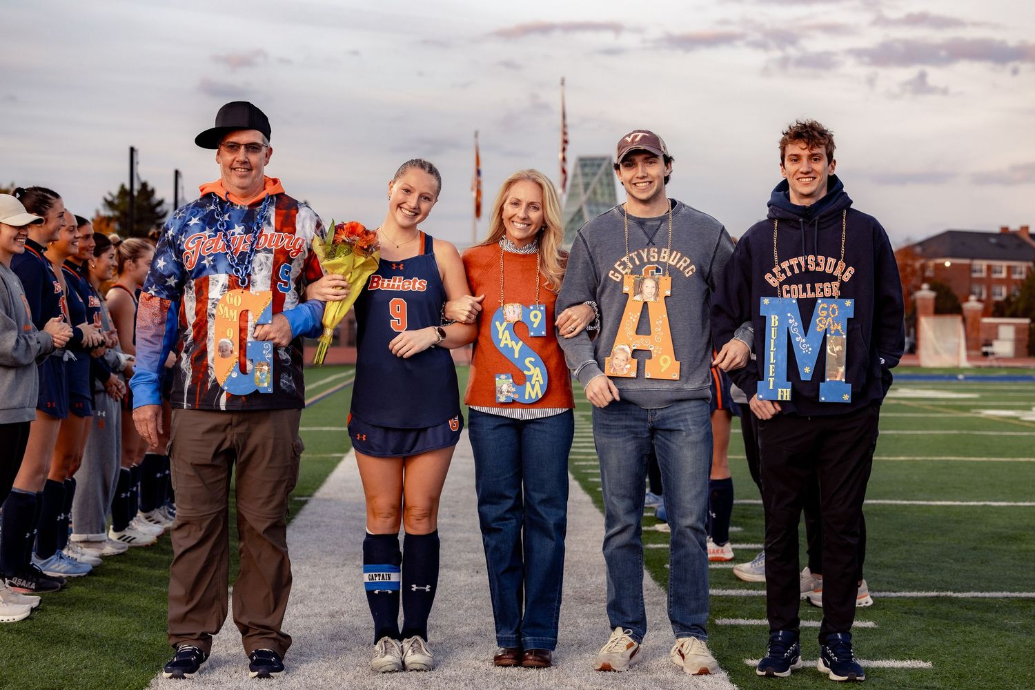 A group of people stand together in a row on a football field during a sporting event at sunset.