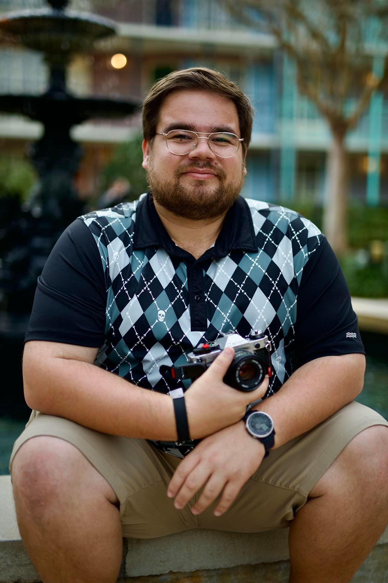 A photographer in an argyle sweater vest sits outdoors holding a camera.
