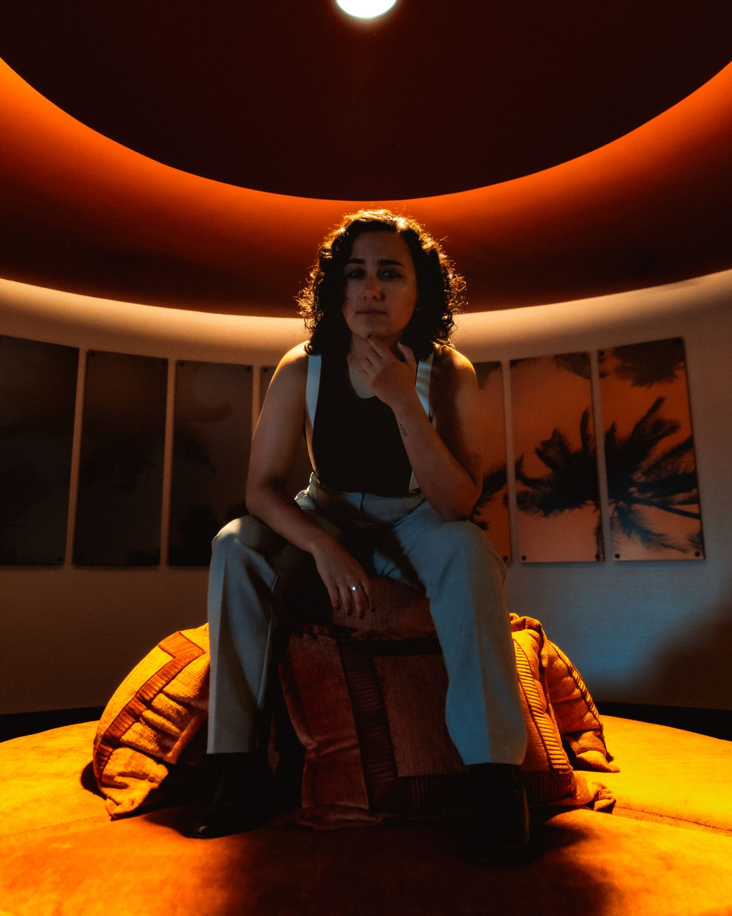 A person sits in an orange-lit circular room creating a dramatic silhouette against curved walls and ambient lighting.
