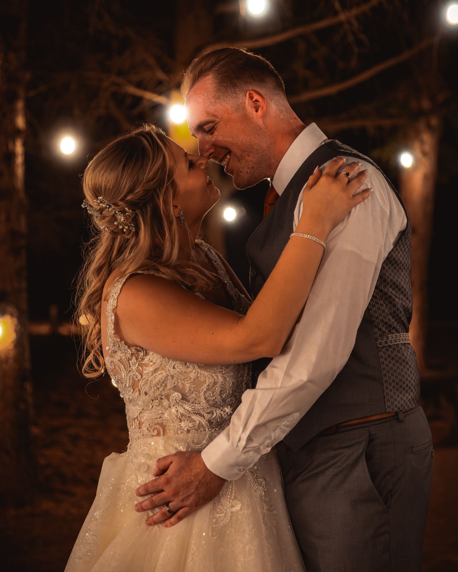 A romantic first dance between newlyweds under warm string lights at an evening outdoor wedding reception.