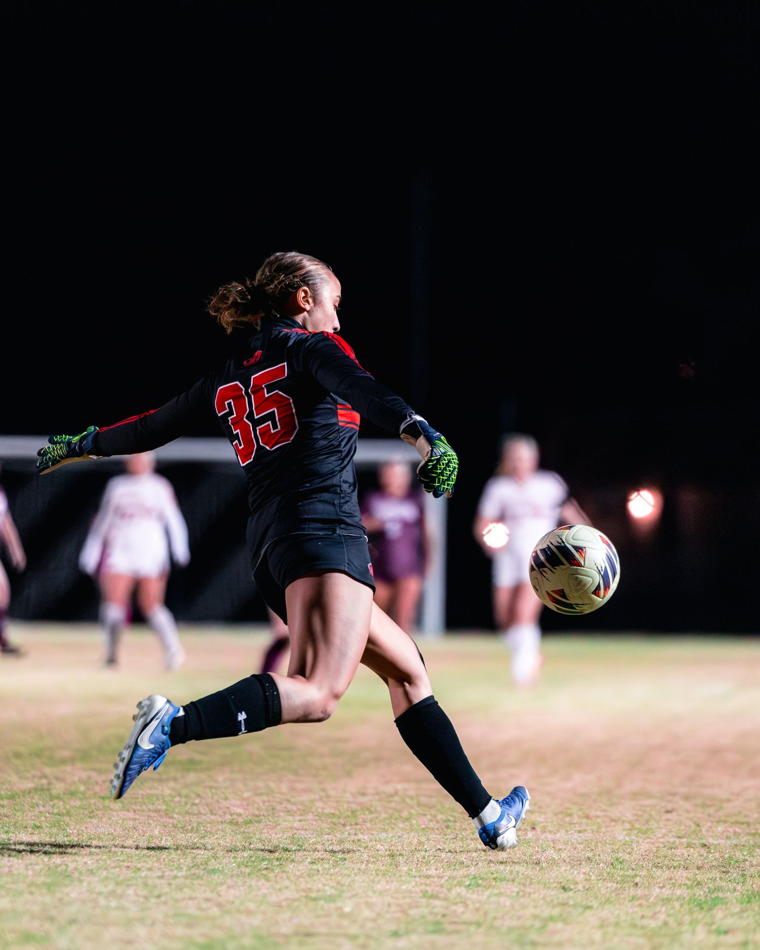 Soccer player diving to make a dramatic save on grass field during night game.
