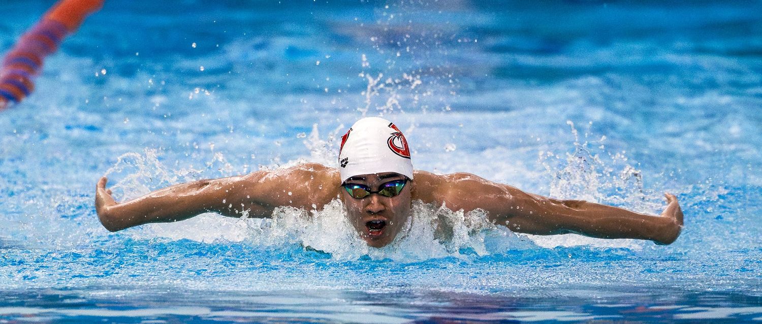 A swimmer performs a butterfly stroke in a pool with splashing water and blue ripples.