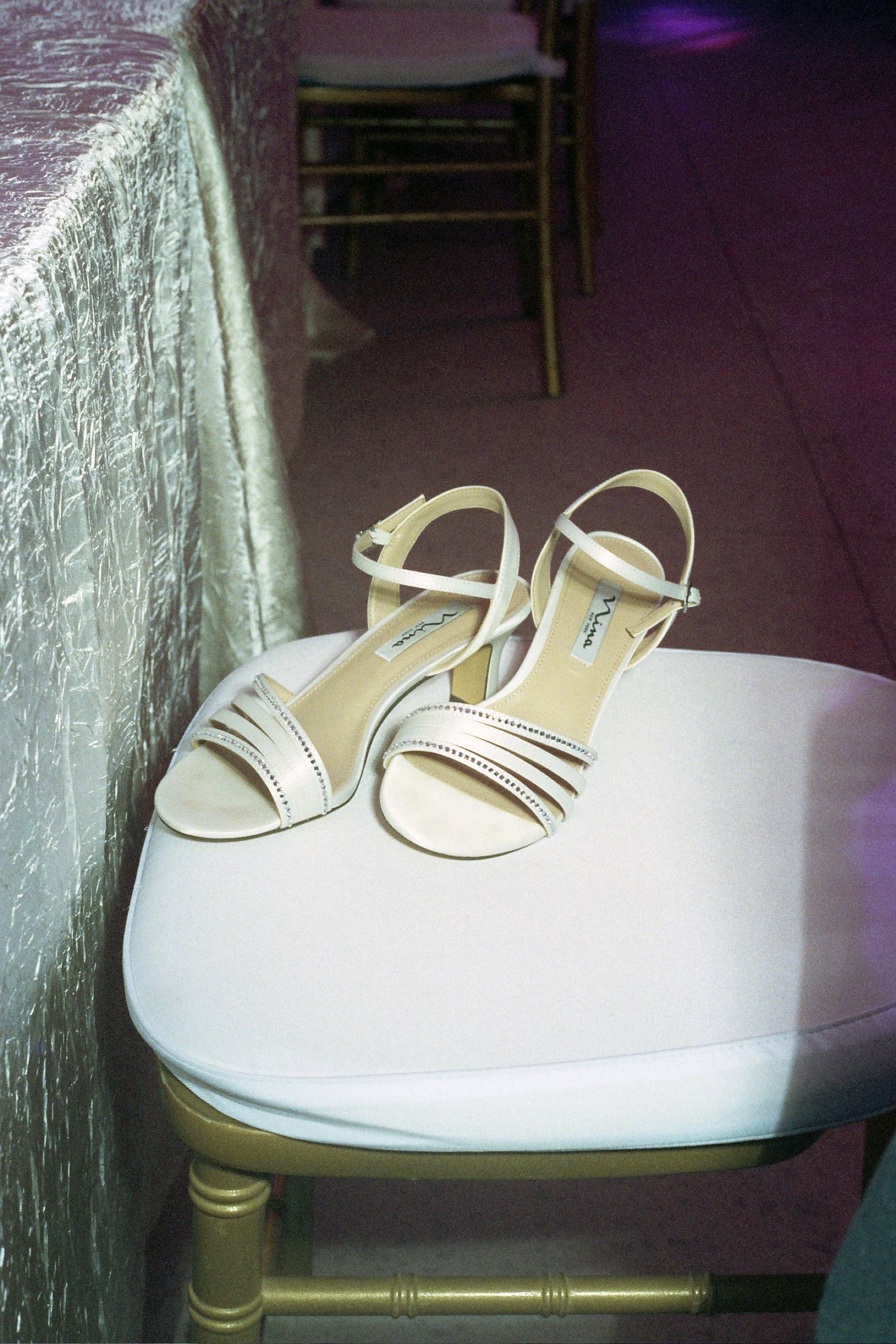 White vintage-style sandals with stripes sit on a rounded table against a purple wall in soft lighting.