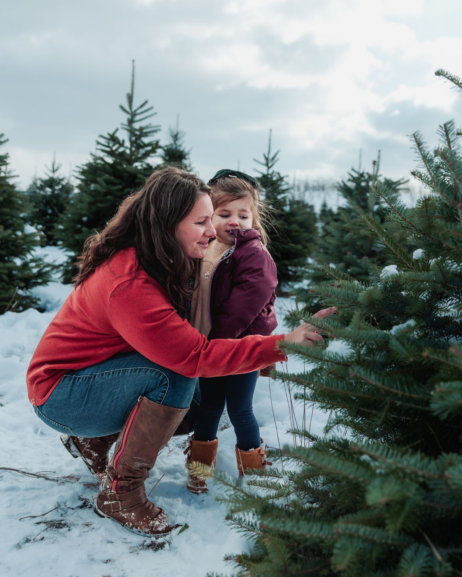 A joyful moment shared between two people in winter attire among snow-covered Christmas trees at a tree farm.