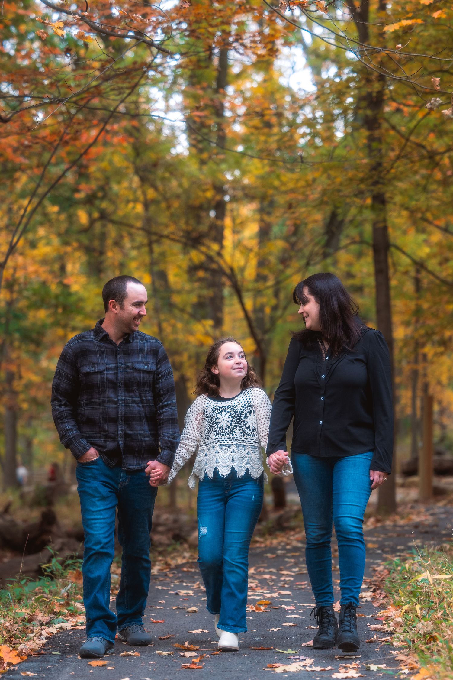A couple walking together through a scenic autumn forest path with colorful fall foliage in the background.
