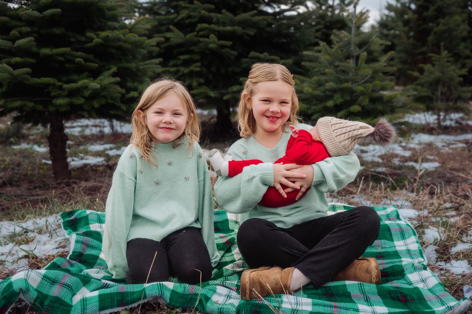 Two people share a cozy moment on a green plaid blanket in a snowy winter setting.
