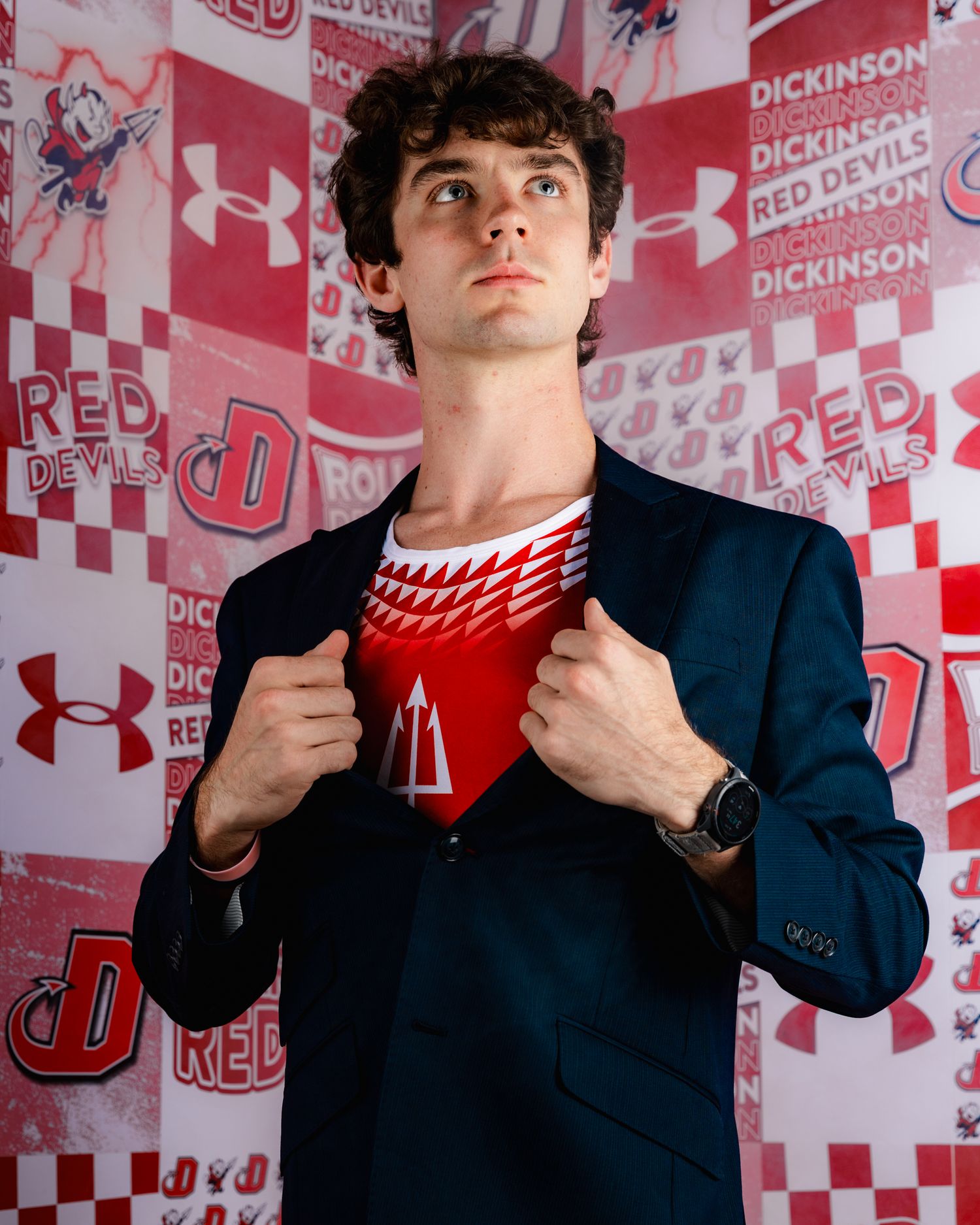 A person in a navy suit adjusts a red and white scarf against a red and white patterned backdrop.