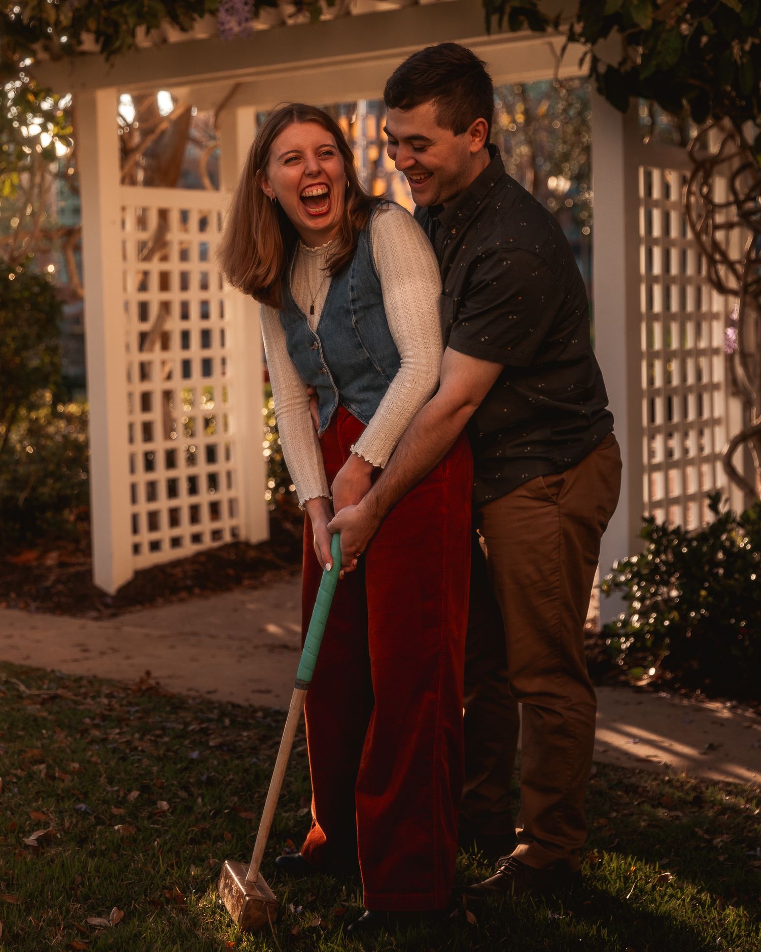 A couple shares a playful moment while holding golf clubs on a romantic evening with twinkling lights in the background.