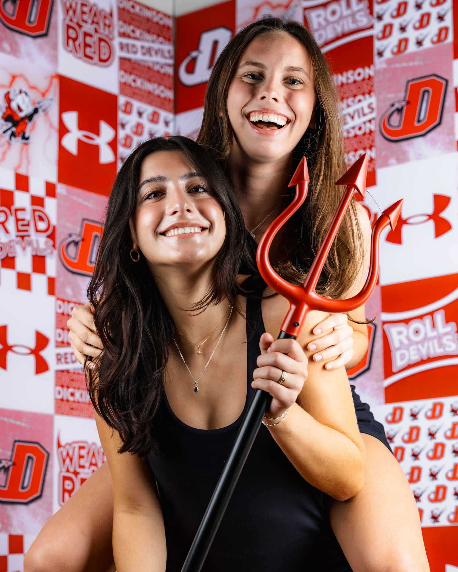 Two people pose with a red pitchfork against a red and white Under Armour branded backdrop.