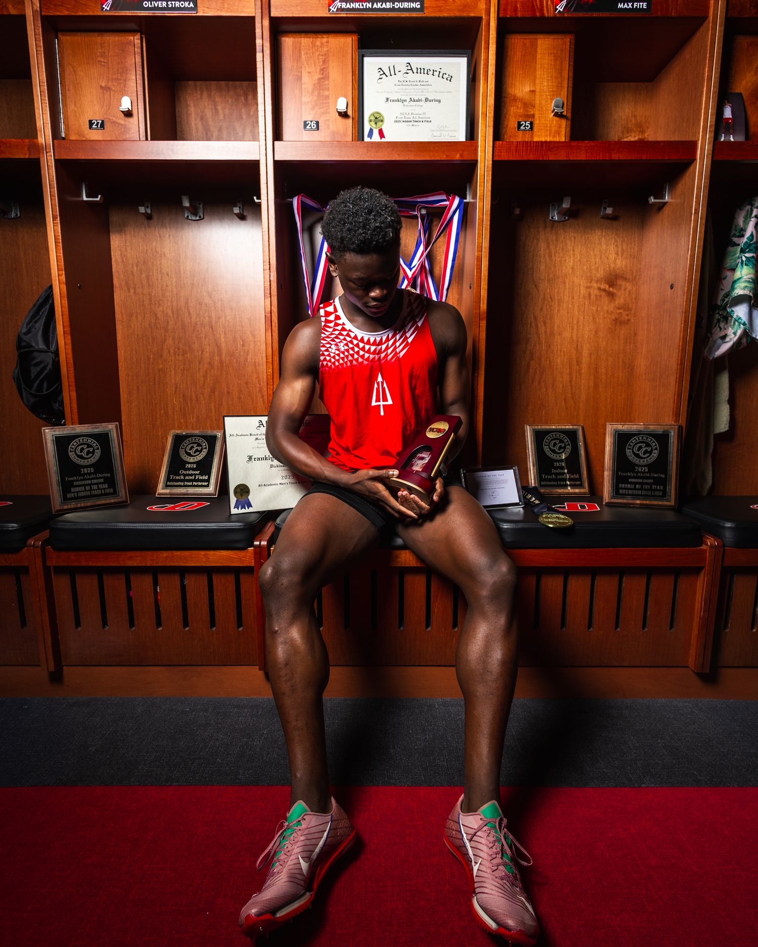Professional athlete sits in locker room wearing red jersey while checking mobile phone before game.