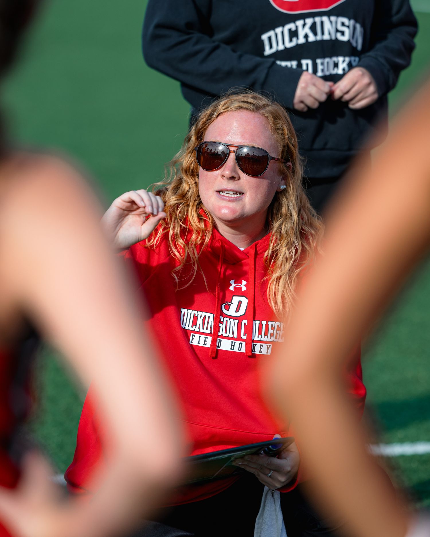 Student wearing sunglasses and a red college sweatshirt sits outdoors on a sunny day.