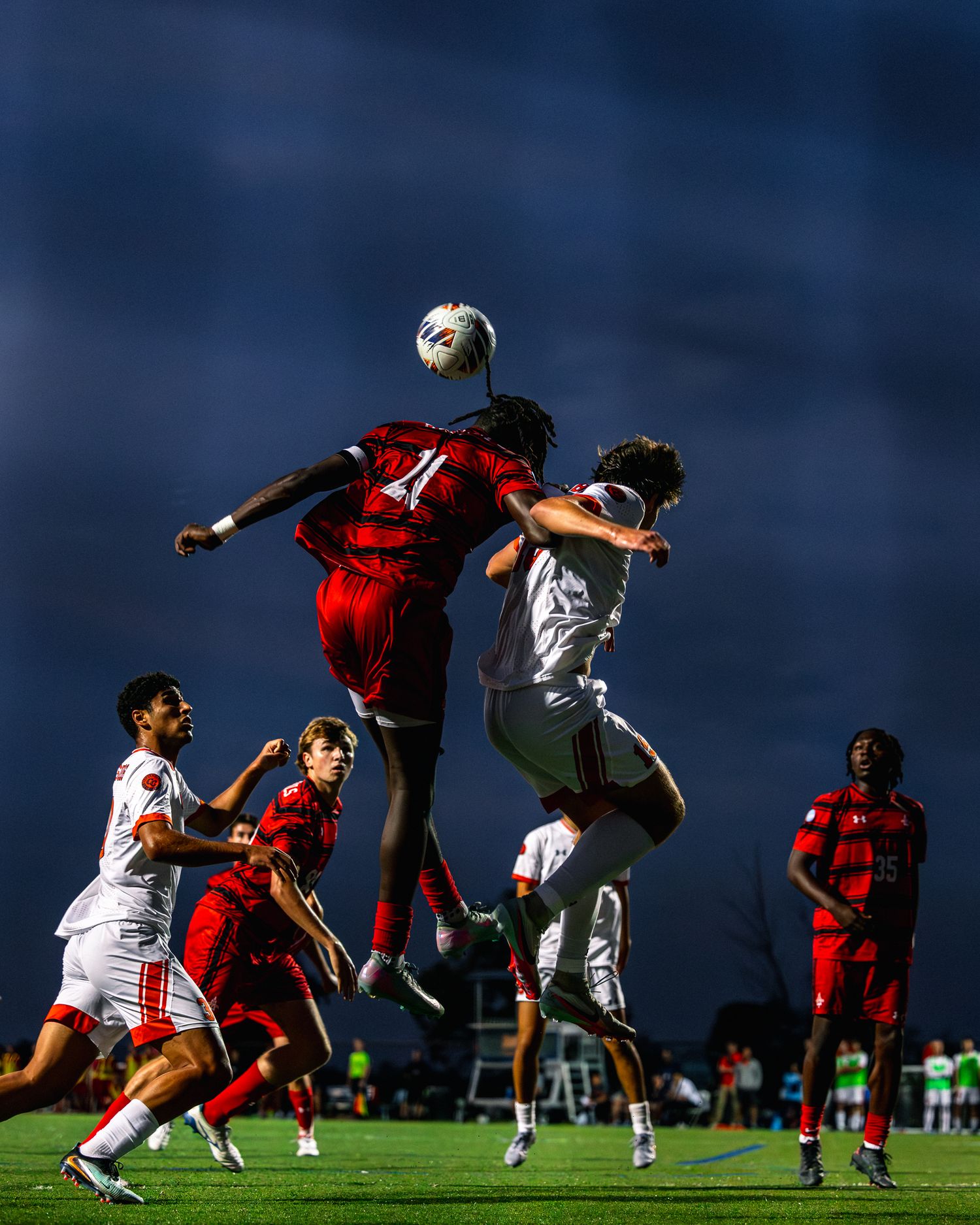 Dramatic soccer match sequence showing players jumping and colliding during an intense aerial battle for the ball.