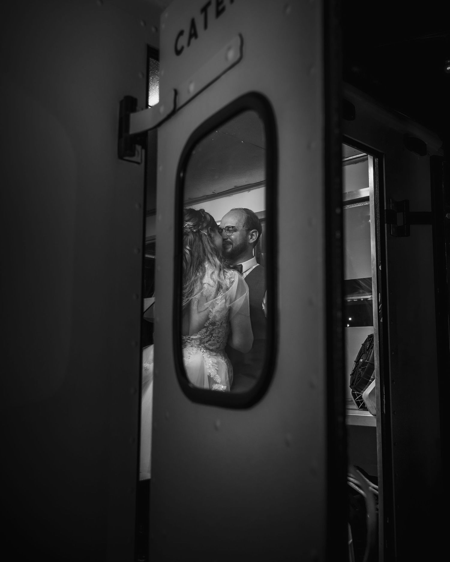 A black and white photograph showing two silhouettes embracing through a train window at night.