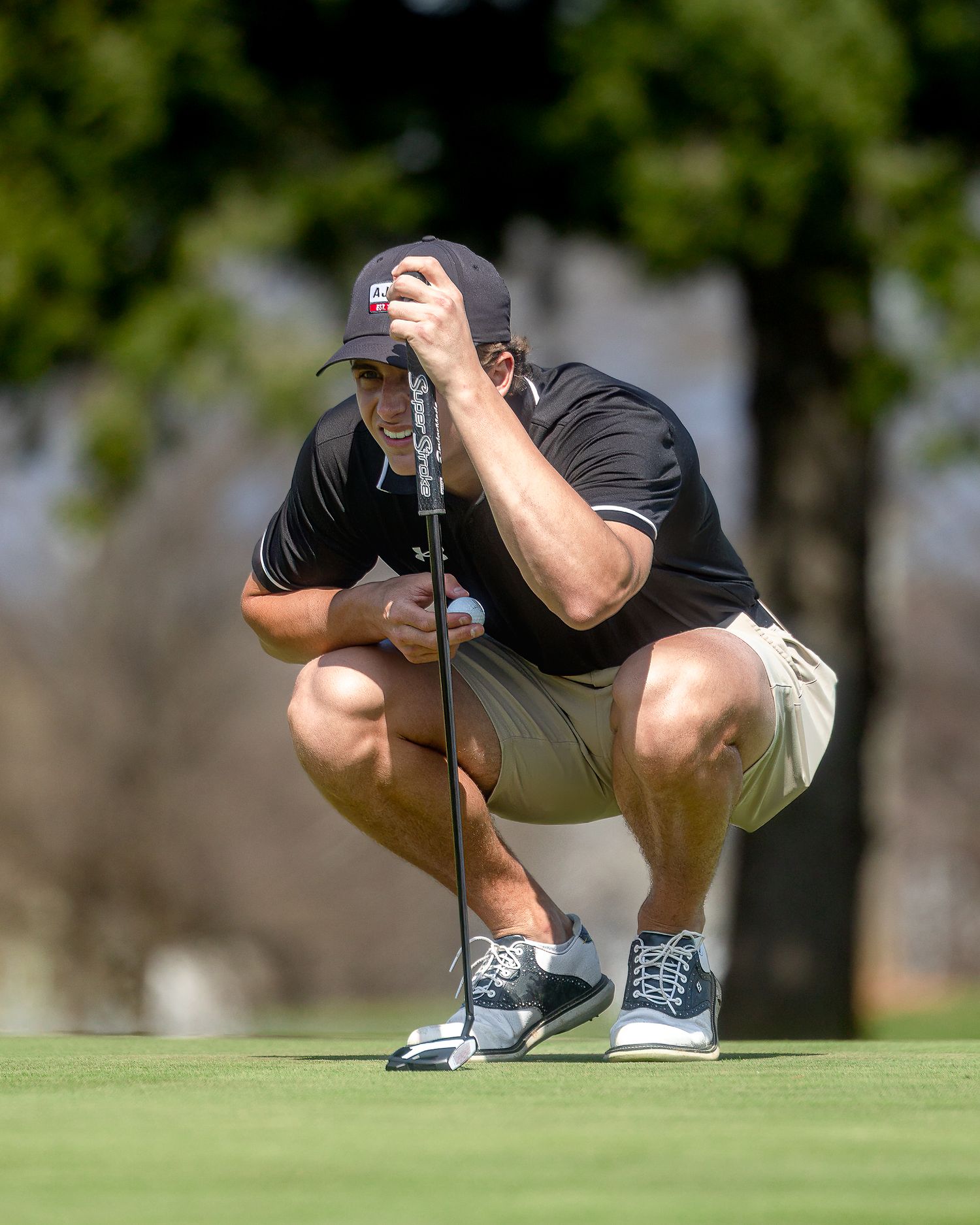 Golfer in black shirt crouches down to read the green before making a putt on the golf course.