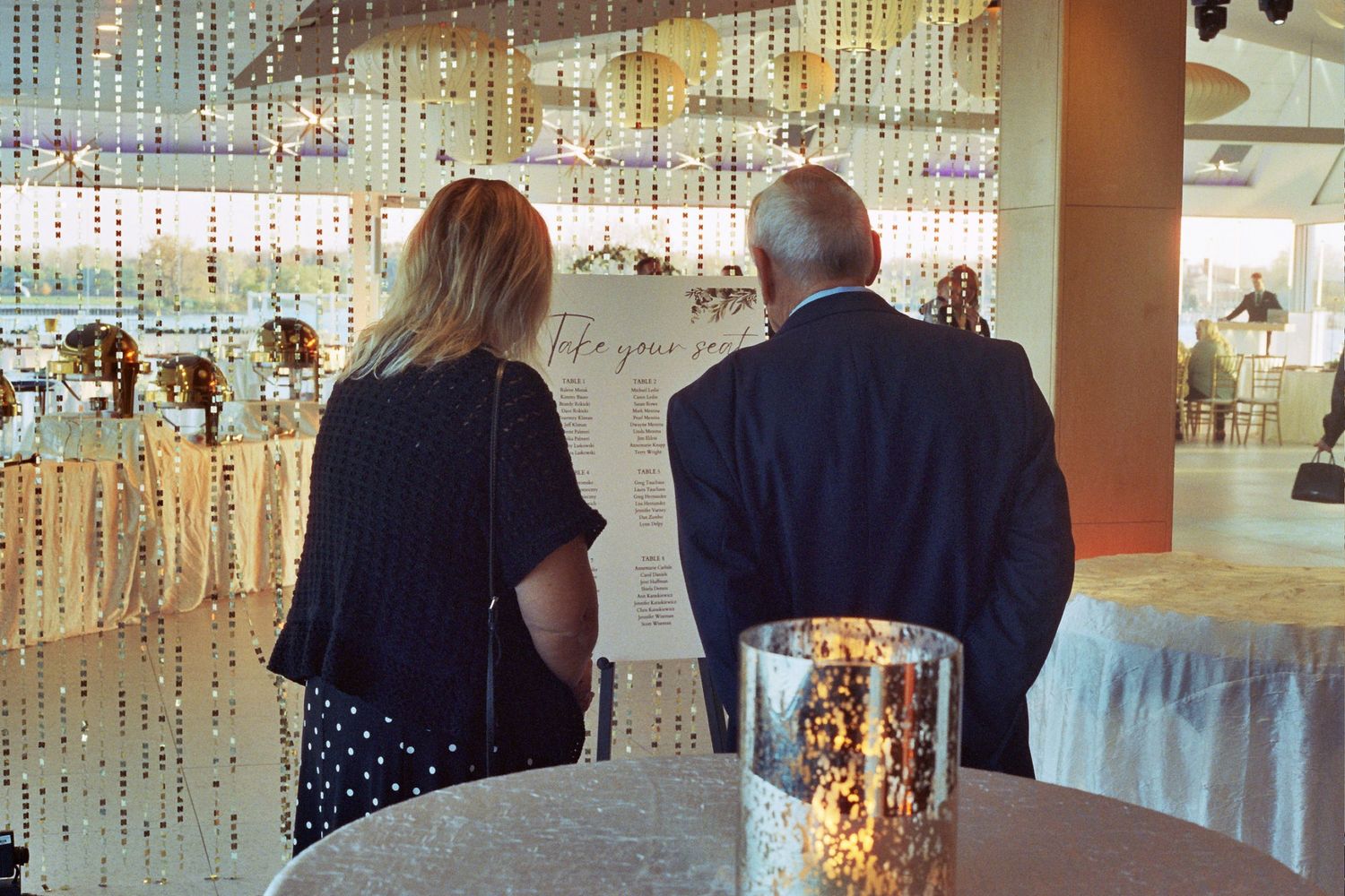 People walking through a modern shopping mall with glass storefronts and bright lighting visible in the reflection.