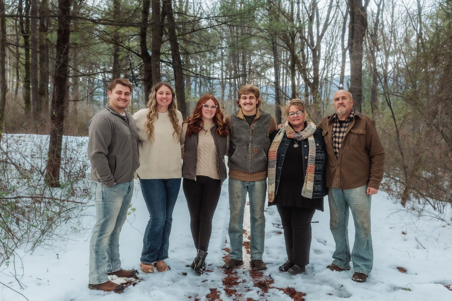 A group stands together in a snowy winter forest setting wearing casual cold weather attire.