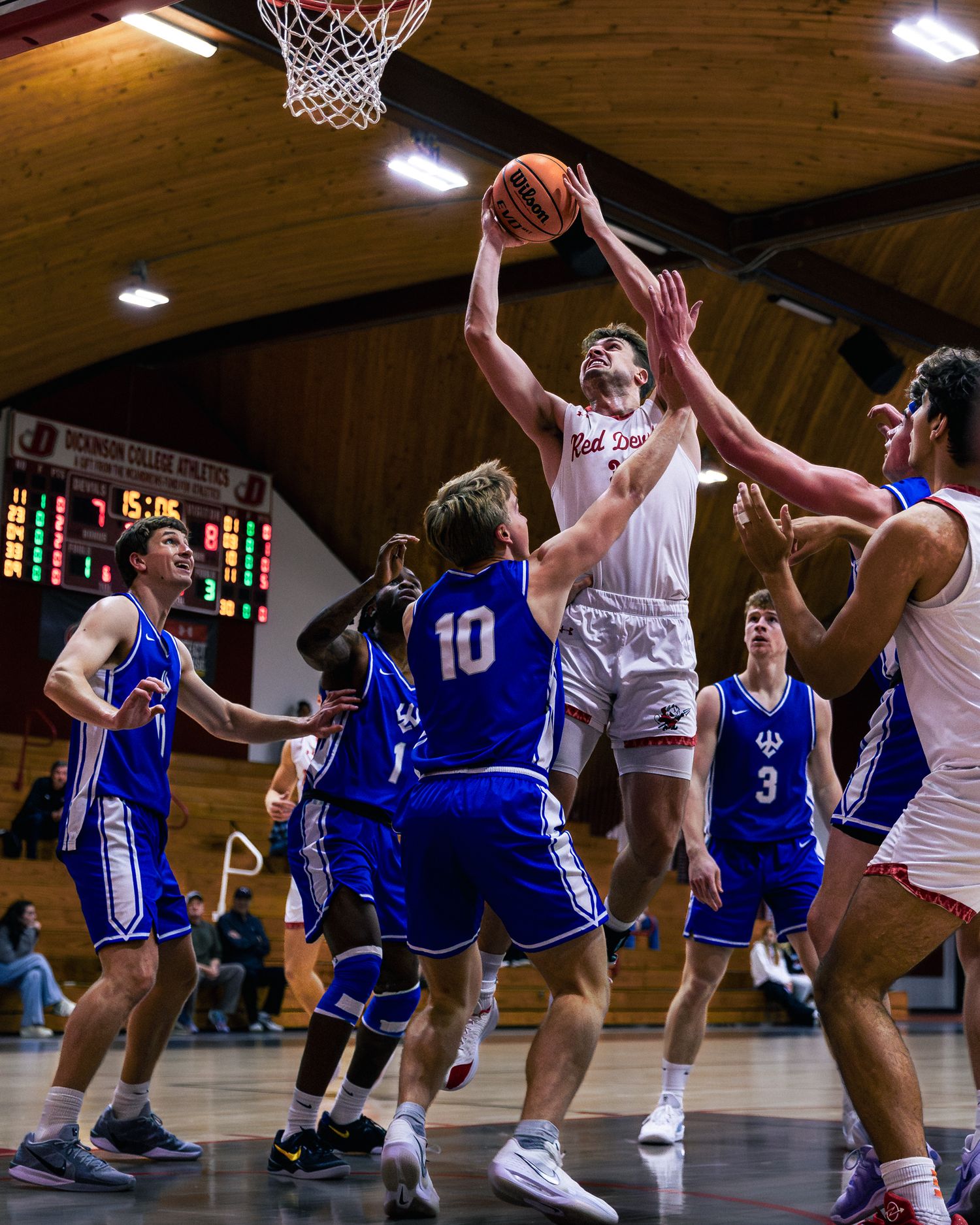 Basketball players in white and blue jerseys compete intensely during an indoor game.