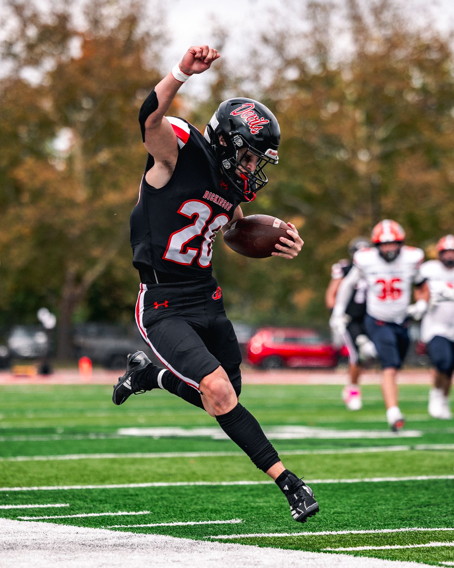Football kicker in black uniform follows through on kick attempt during game on artificial turf field.
