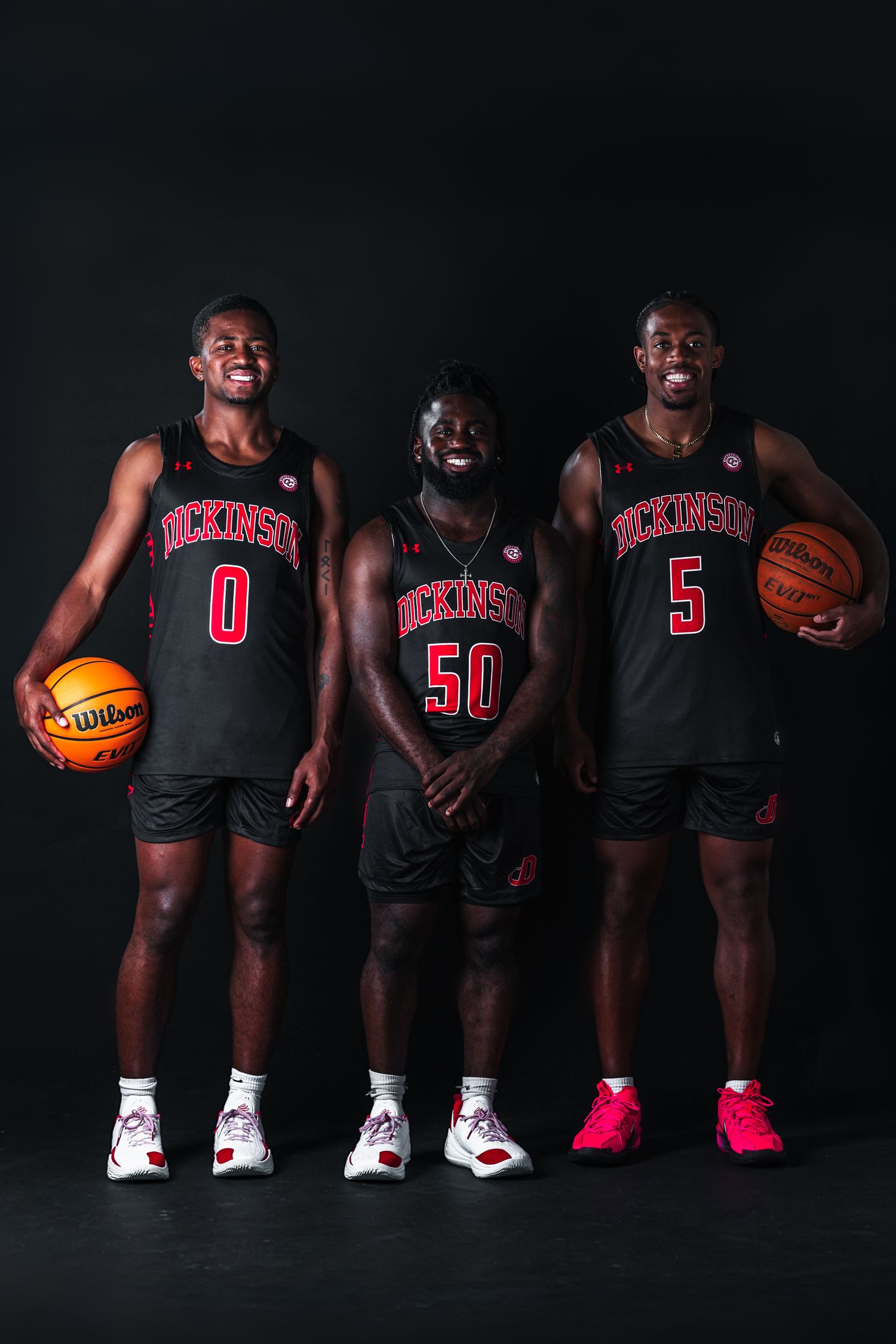 Basketball players in black uniforms with red accents pose for a dramatic team photo against a dark background.