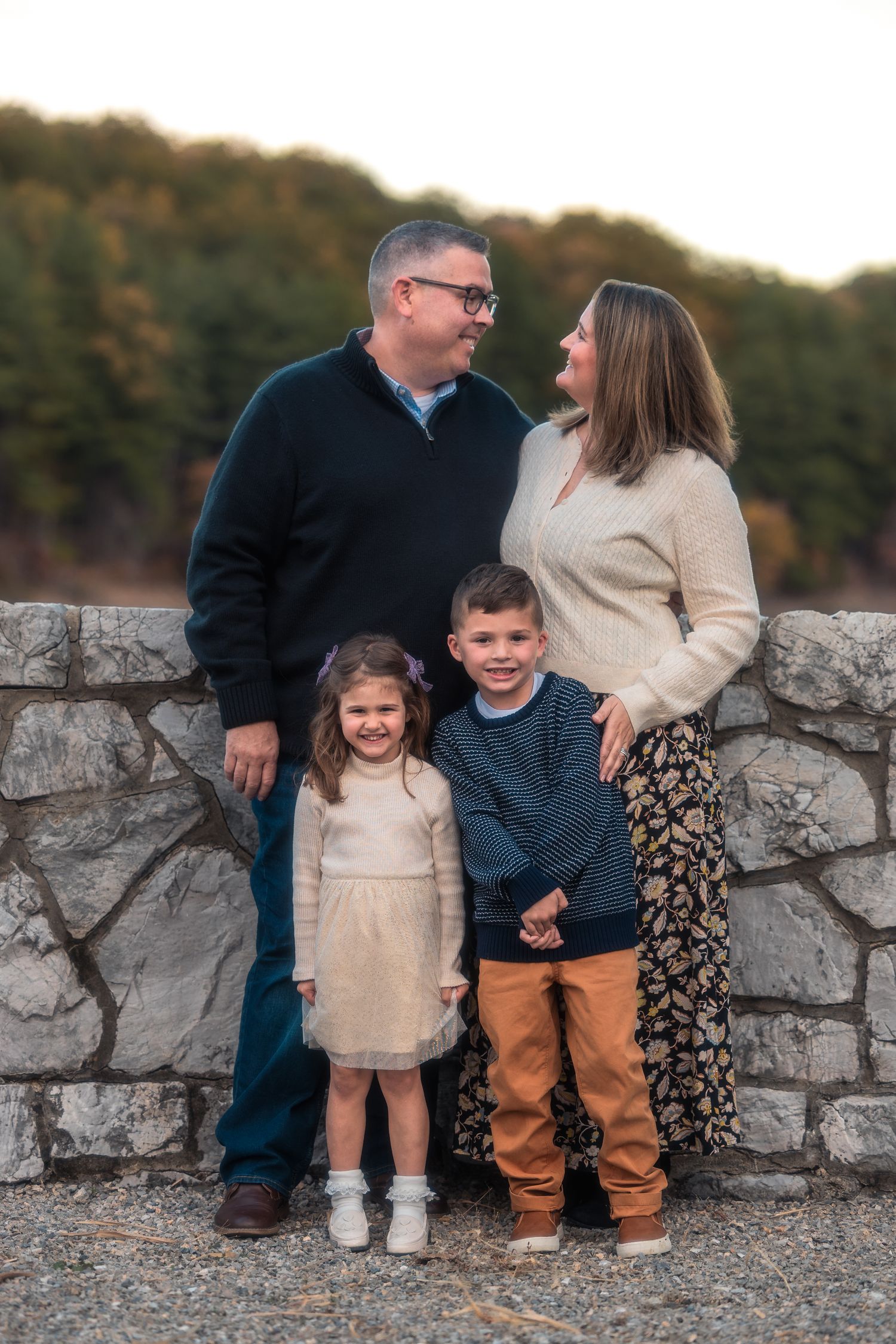 Family in coordinated outfits leaning against stone wall during outdoor autumn photoshoot.