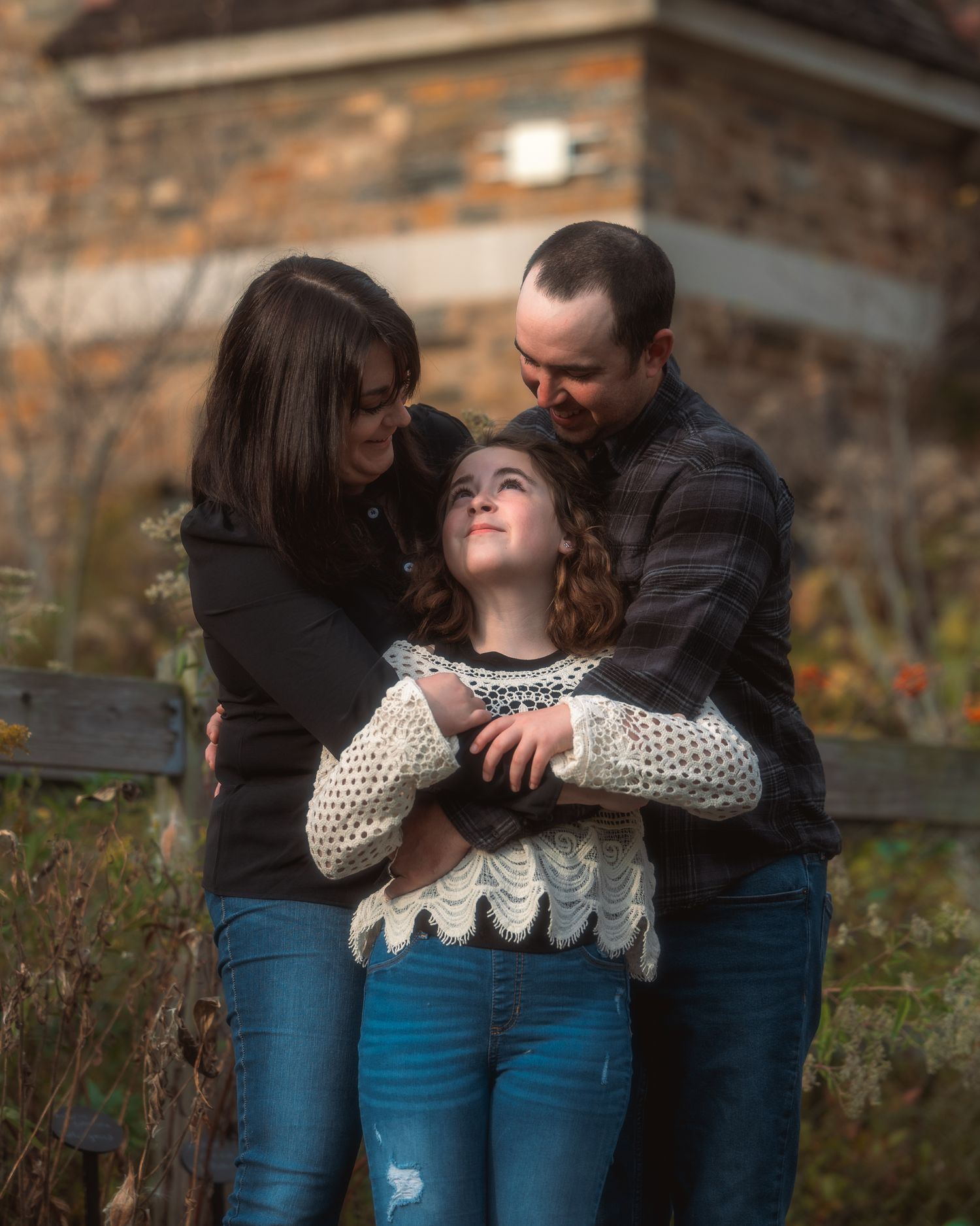 A family shares an intimate moment together outdoors on an autumn day, embracing and smiling in casual attire.