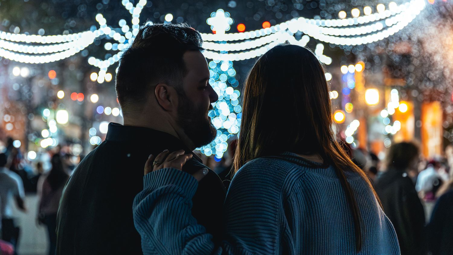 Couple viewing holiday lights display at night with blue decorative lighting.