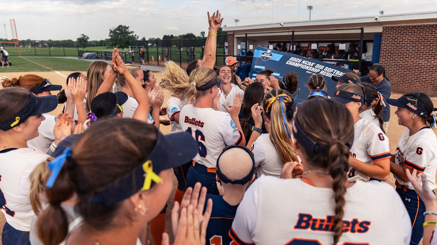 Sports team celebrates with hands raised in victory huddle on field.