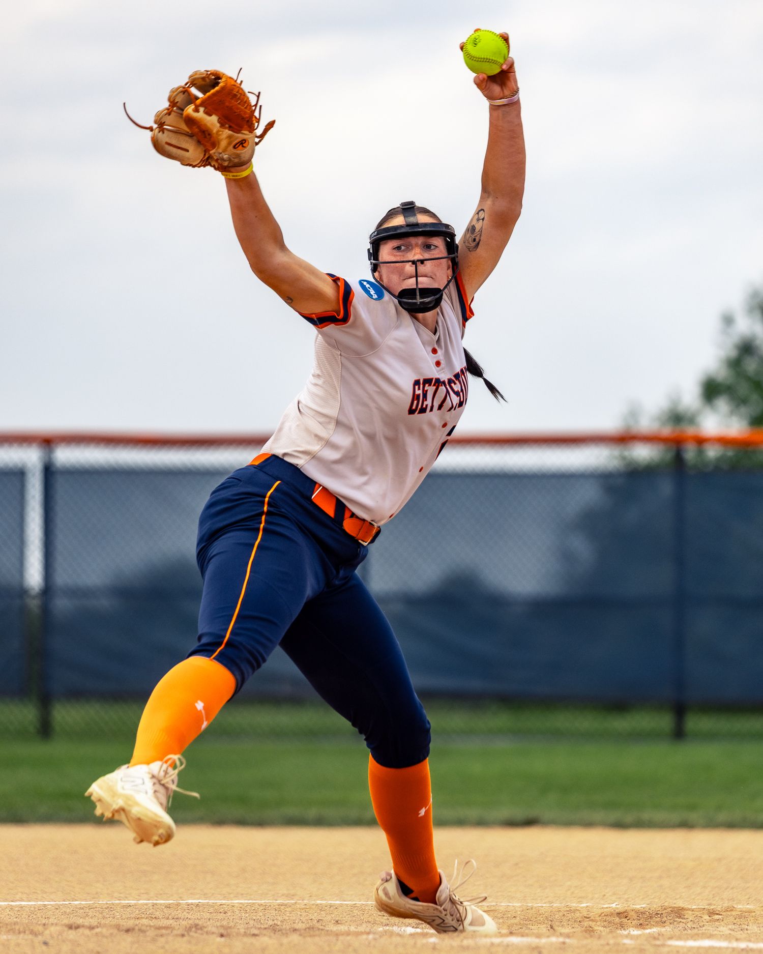 Softball player in navy and orange uniform leaping to catch a ball during a game.