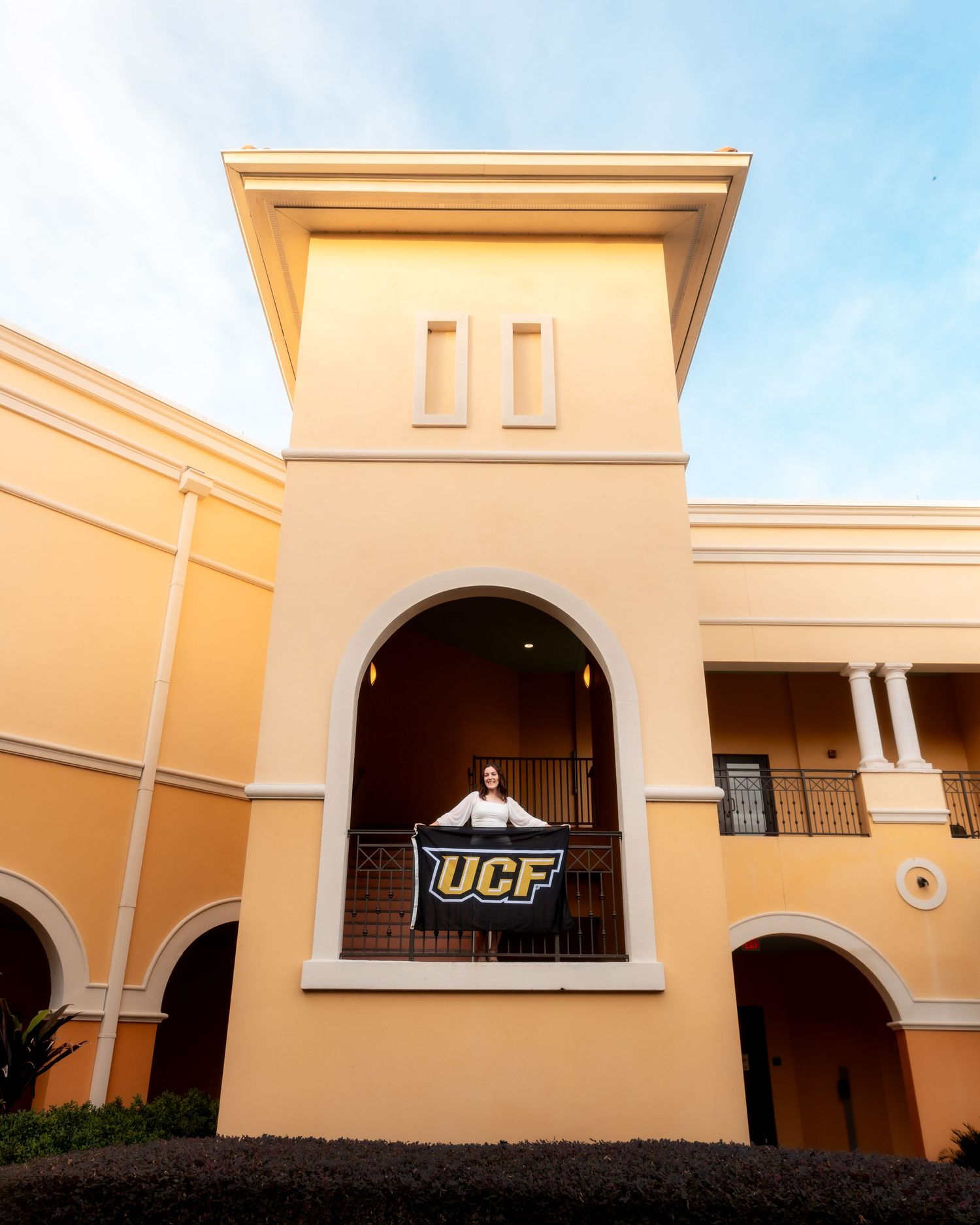 A series of connected beige stucco buildings with arched doorways and a UCF logo sign mounted on one wall.