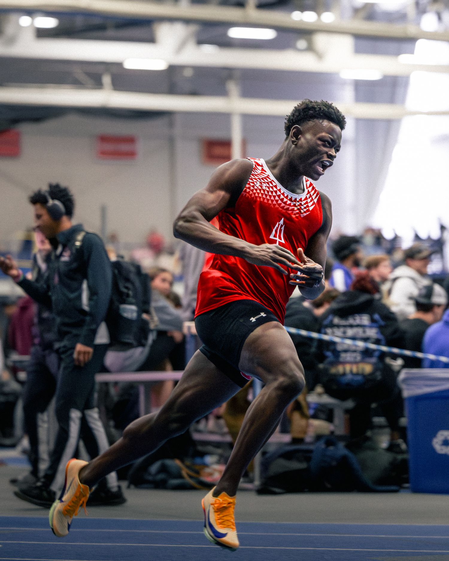 Track athlete in red jersey performs powerful long jump at indoor competition, captured in motion sequence.