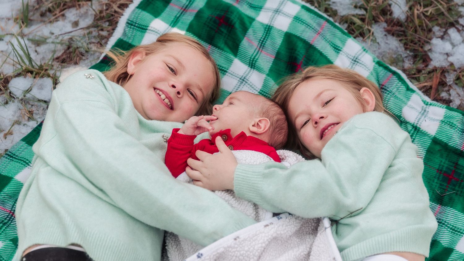 Two people laying side by side on a green and white checkered blanket in winter.