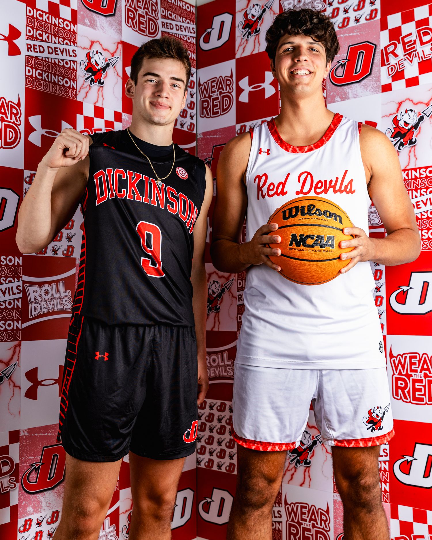 Basketball players pose in front of a red and white branded backdrop with Red Devils logos and graphics.