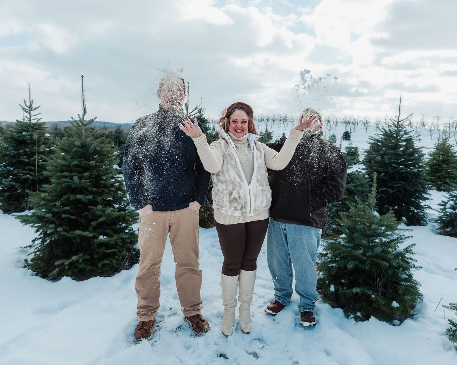 People walk through a snowy Christmas tree farm searching for the perfect evergreen tree on a cloudy winter day.
