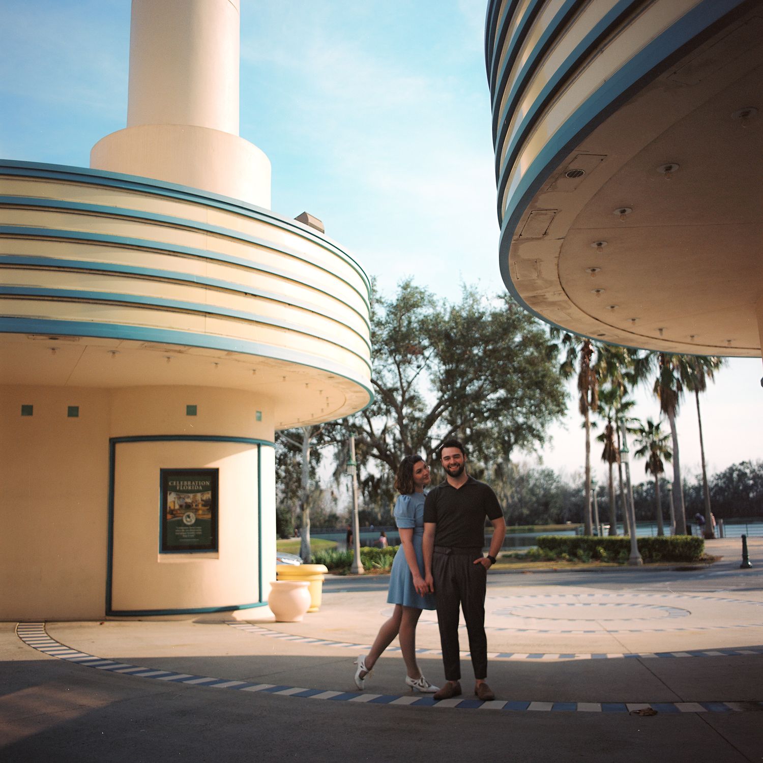 A curved colonnade with teal stripes wraps around a modern building exterior against a cloudy sky.