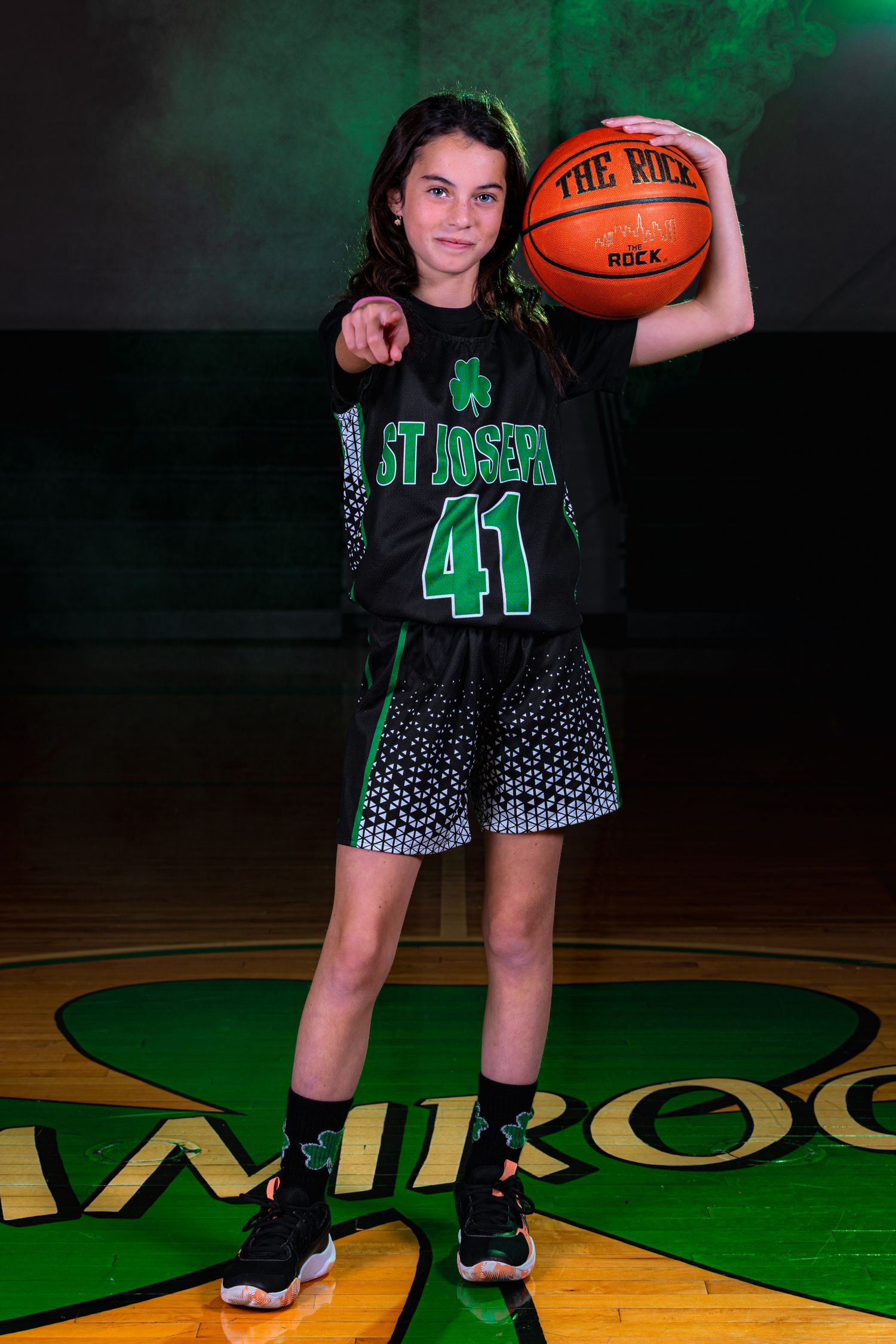 Basketball player in black and green uniform with number 41 poses in front of dark background with green lighting.