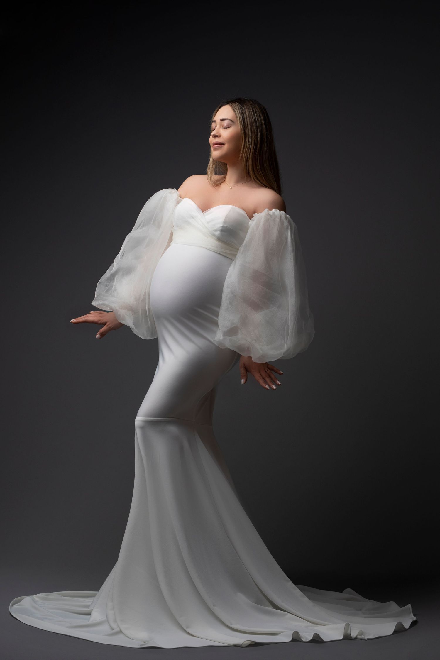 Dramatic maternity gown with puffy white sleeves and mermaid silhouette against dark backdrop. Dubai Photographer