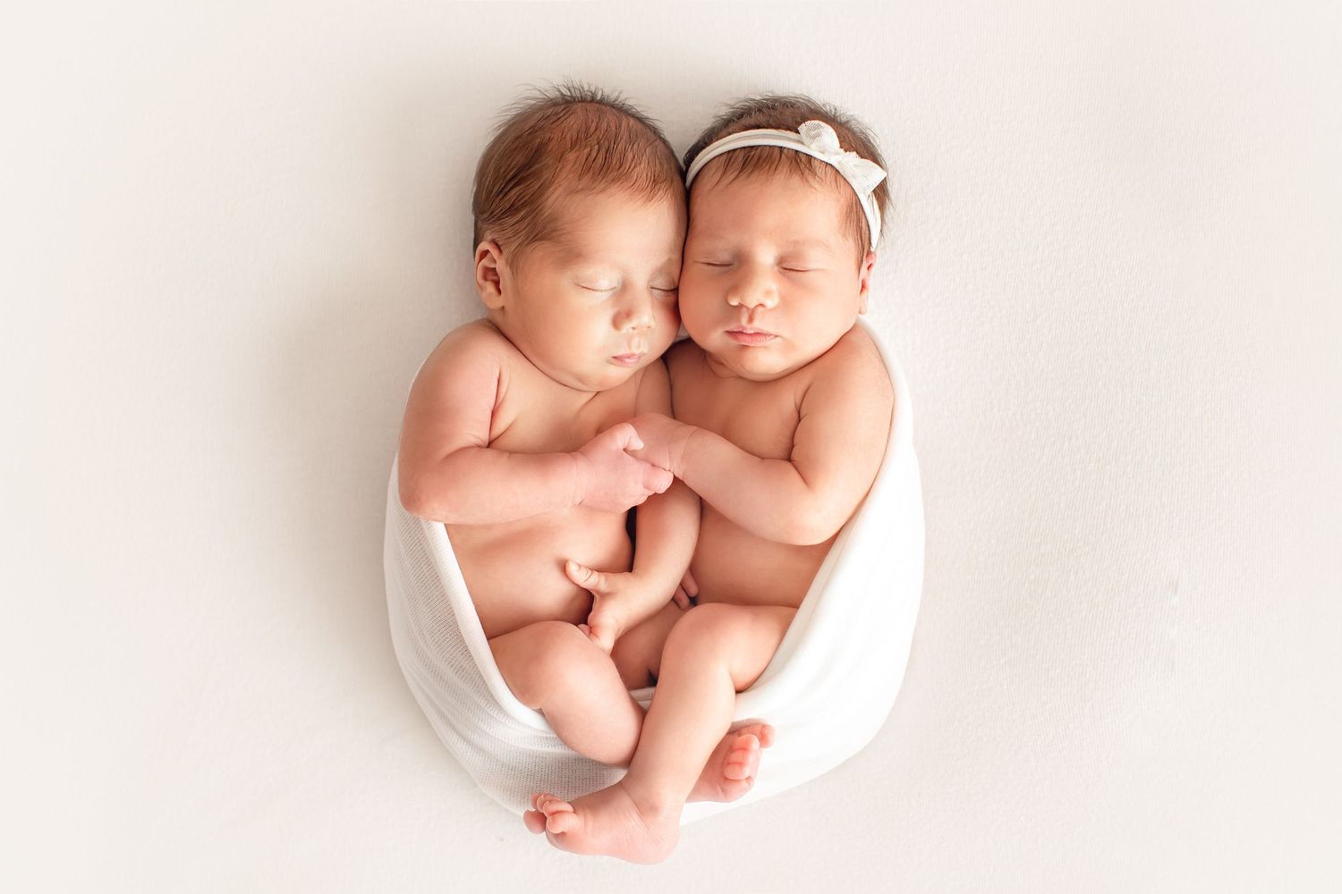 Twin newborns cuddled together in white bowl against neutral background. Dubai Photographer