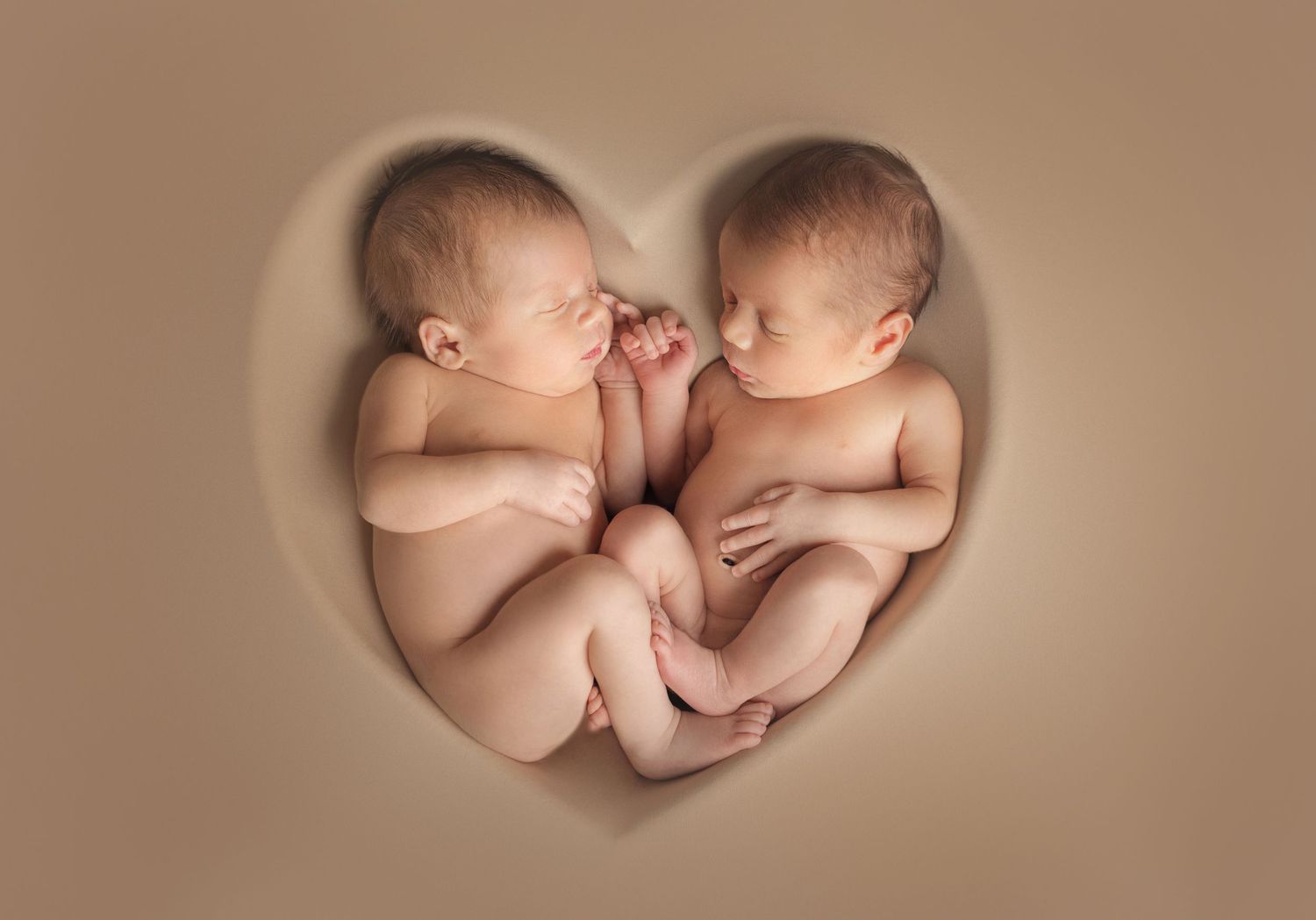Two sleeping newborns positioned in heart shape on beige background. Dubai Photographer