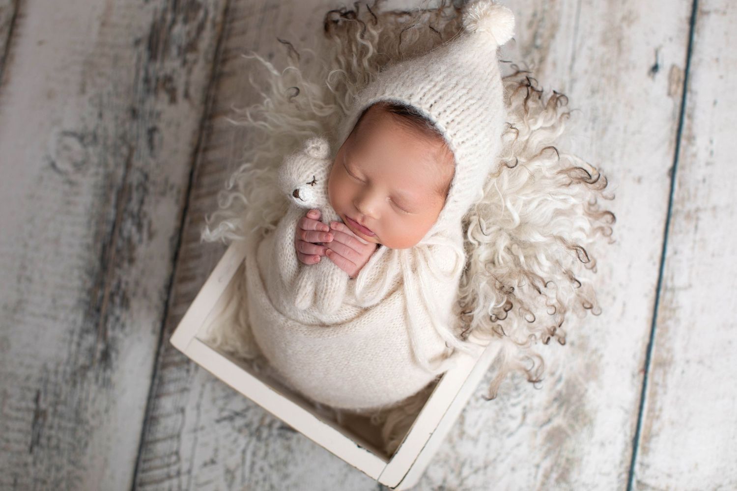 Sleeping newborn in white knit hat and wrap nestled in wooden box. Dubai Photographer