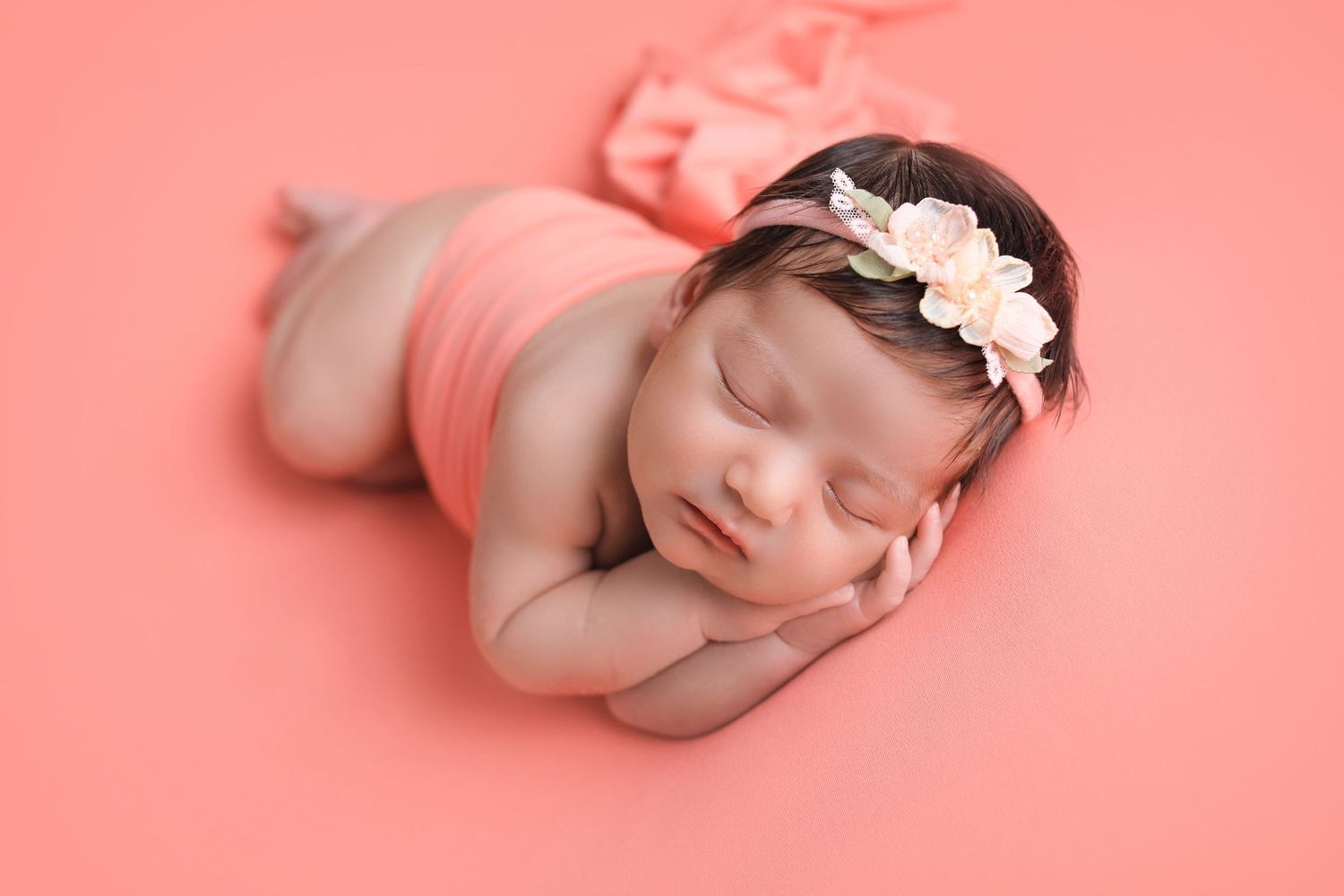 Newborn photography of sleeping baby on pink backdrop wearing floral headband. Dubai Photographer